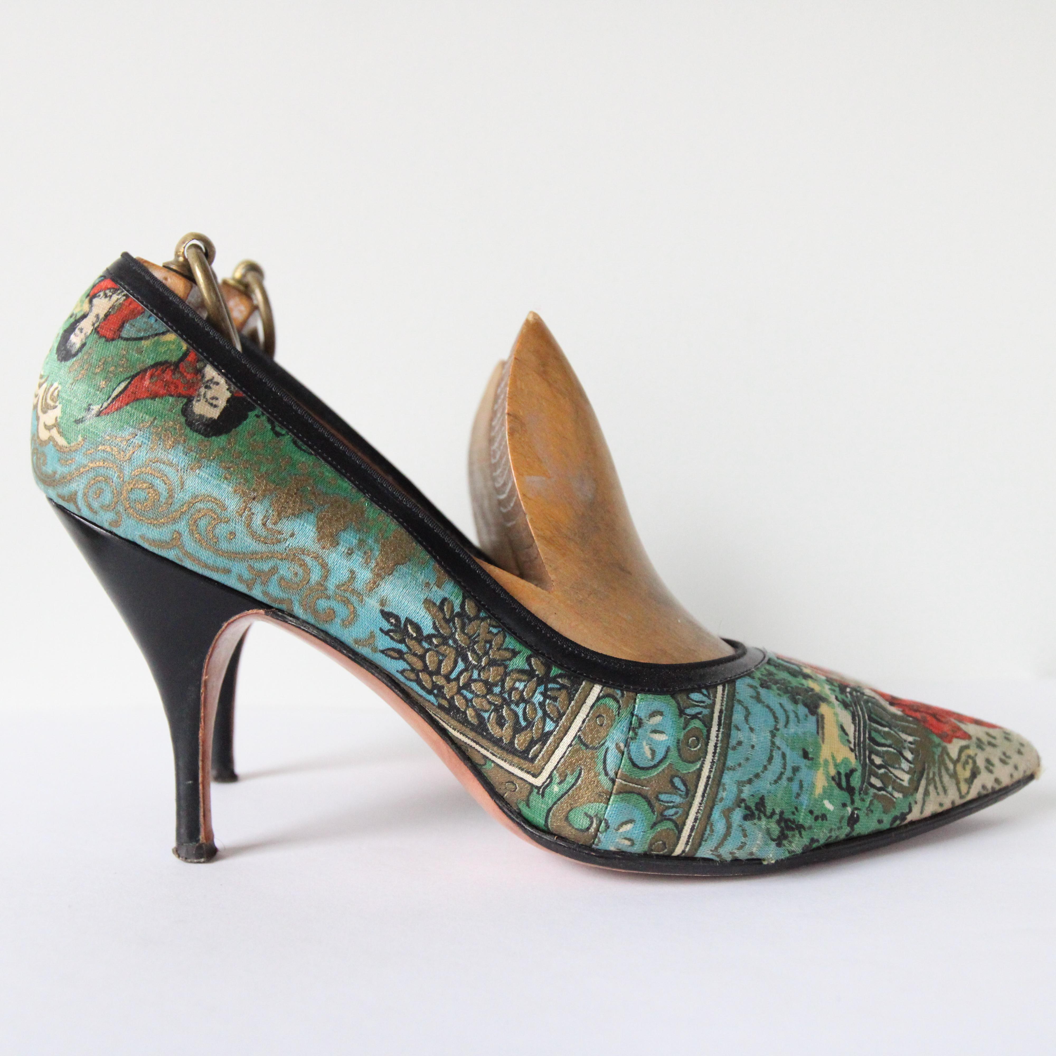 Rendered in the most eye-catching hand printed silk, depicting a woman in a Victorian red dress, surrounded by garden scenes in shades of blue, green and yellow, and accented with gold toned finishes, this breathtaking pair of 1950's stilettos are