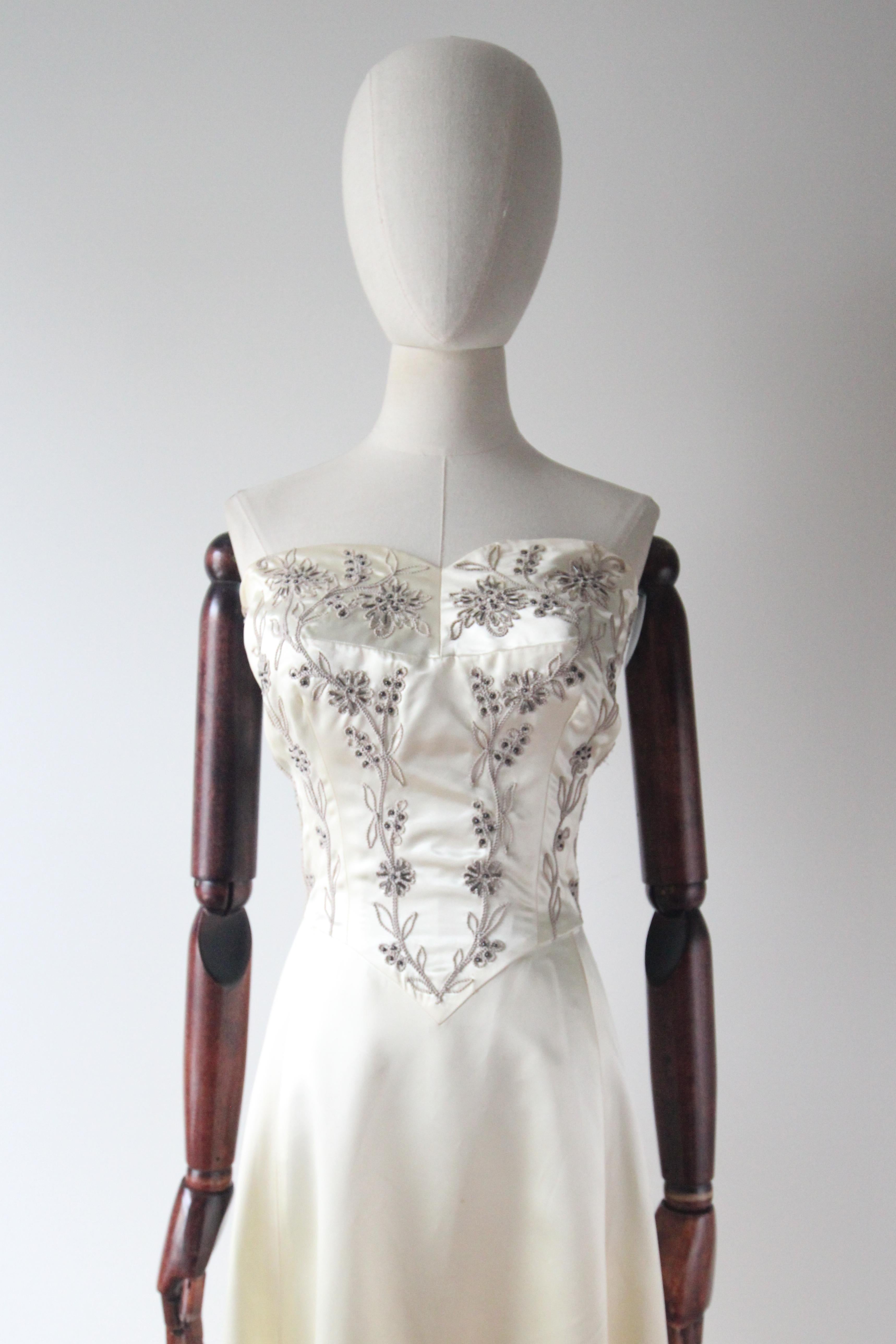 This truly majestic 1950's Frank Starr for Ted Shore gown, rendered in a beautiful cream satin and embellished with pale grey soutache embroidery and grey toned glass beadwork in a trailing floral design, is the perfect piece for that special
