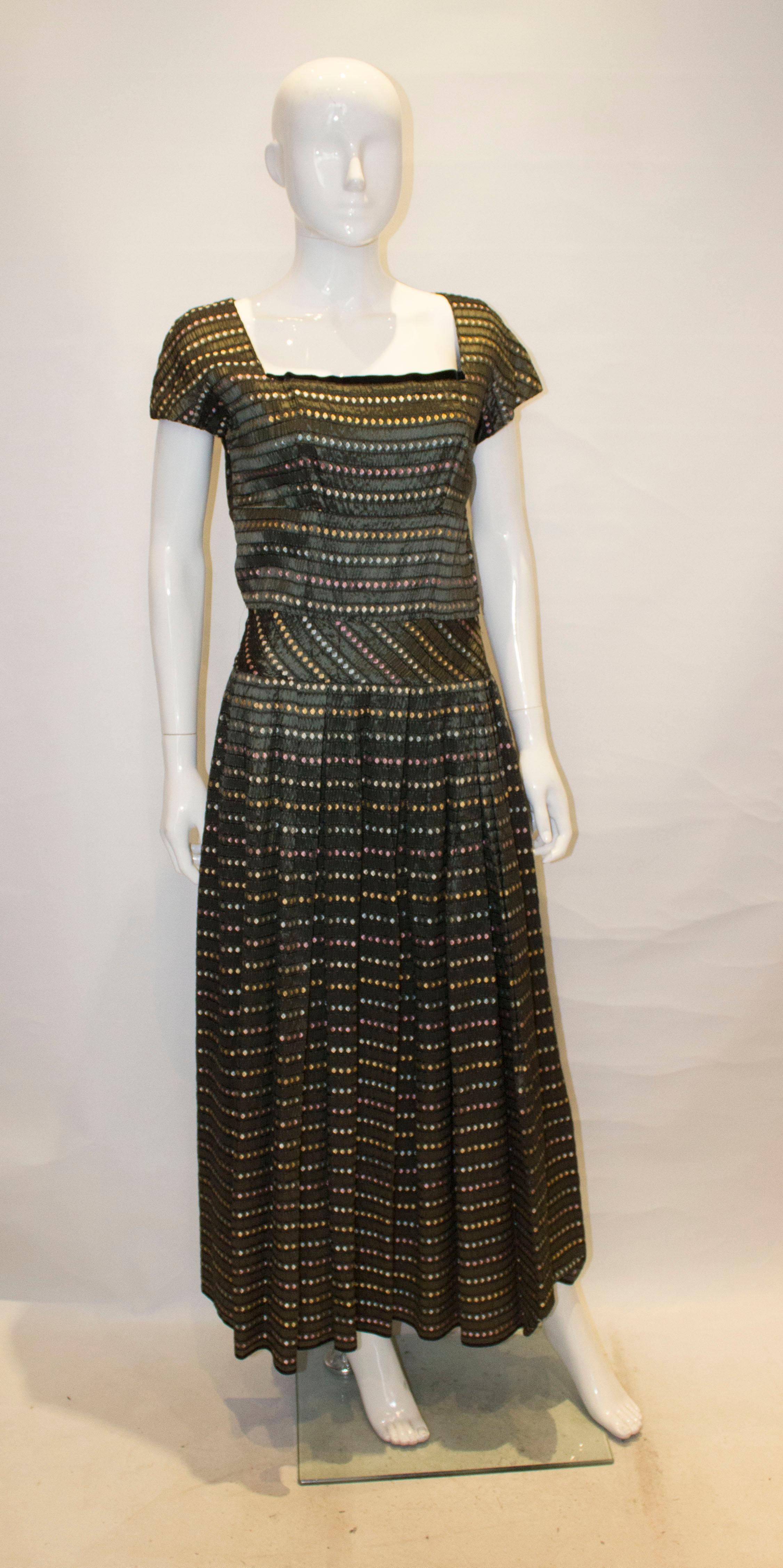 A headturning evening gown from the 1950s by Susan Small.  The dress has an olive /grey background with multi colour horizontal bands., and has a square neckline , cap sleaves and a full skirt.