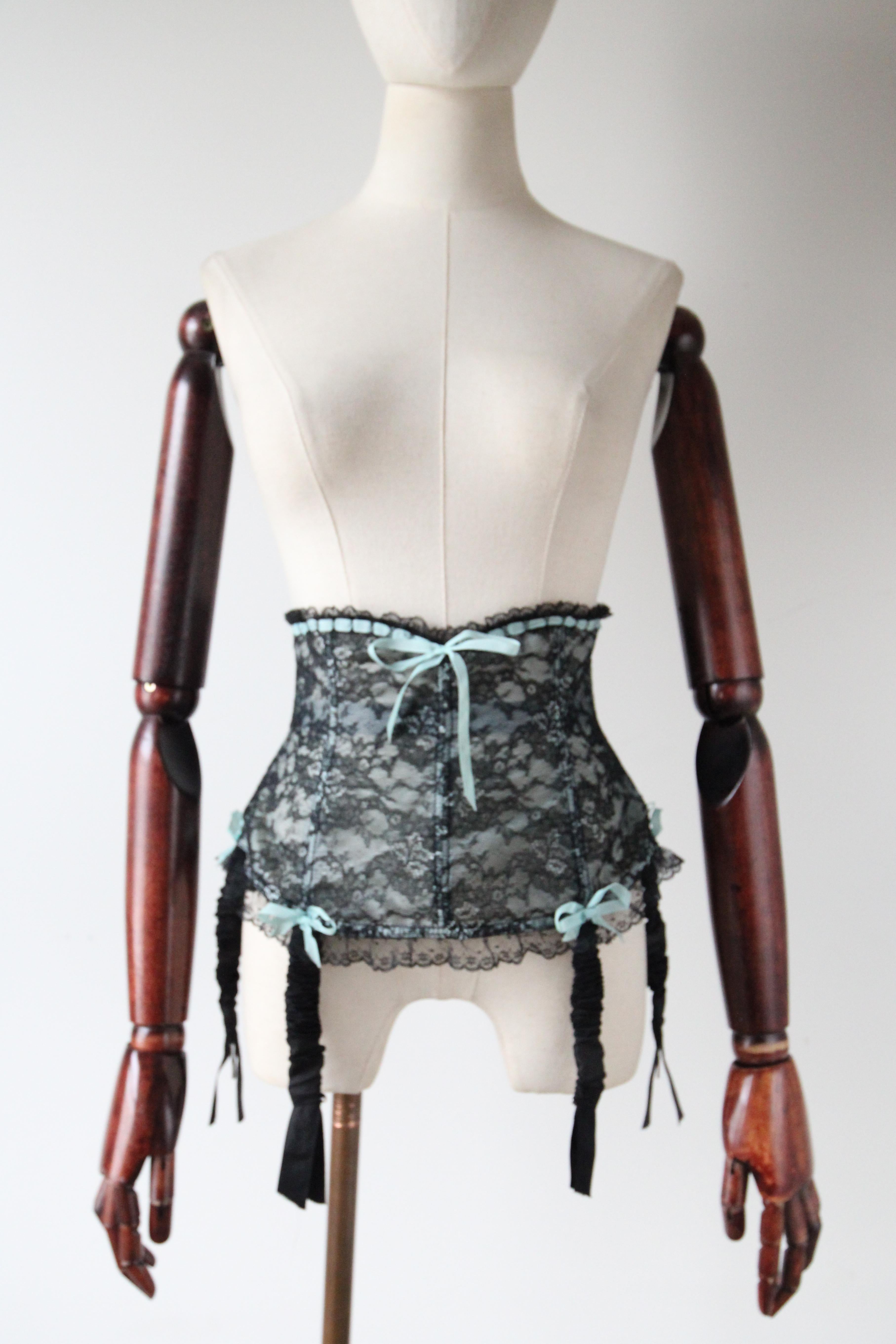 Ce charmant porte-jarretelles des années 1950 en dentelle noire et bleu, avec une dentelle florale, est la pièce parfaite à ajouter à votre collection de lingerie. Le large design waspie du porte-jarretelles est accentué par une doublure en nylon