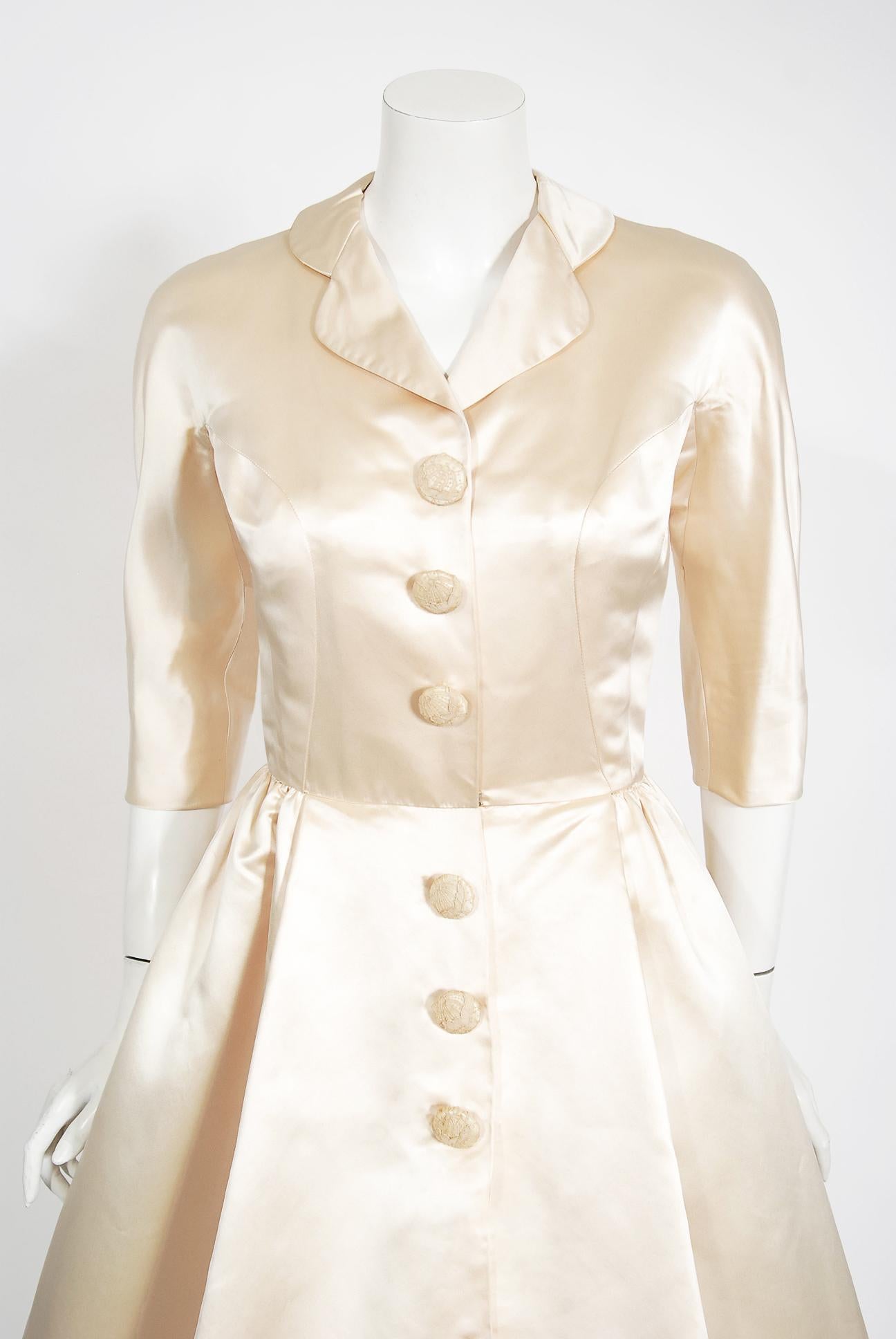 An incredibly chic and totally timeless Traina Norell designer ivory silk satin full-skirted cocktail dress dating back to the mid 1950's. This exquisite Traina-Norell museum quality dress exemplifies their signature blend of couture-level quality