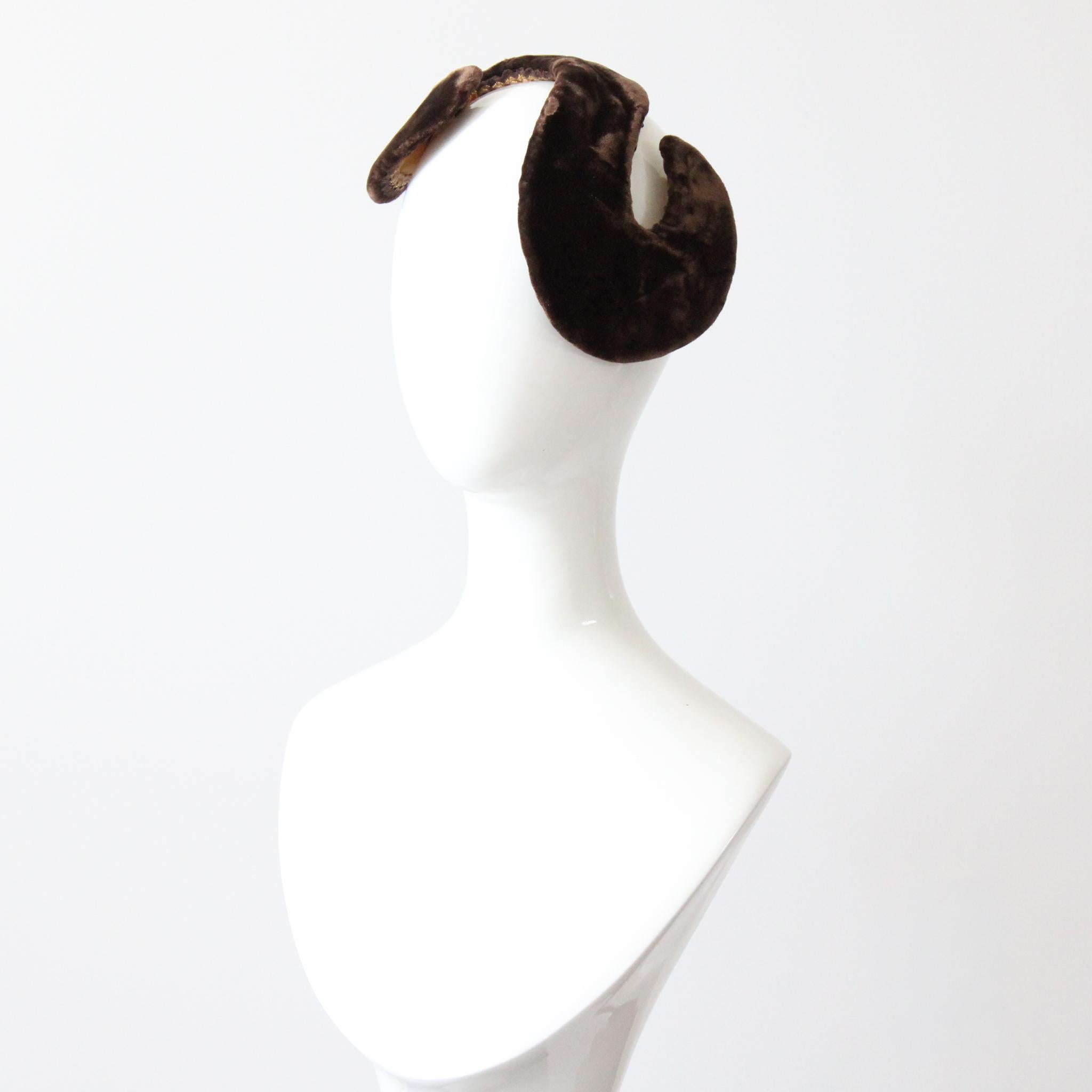 Questo delizioso cappello in velluto marrone cioccolato amaro degli anni '50, a forma di S curva, è un pezzo raro da vedere. La forma scultorea vanta una corona arrotondata e ricurva, bordata internamente con un filo di ferro per mantenere la forma,
