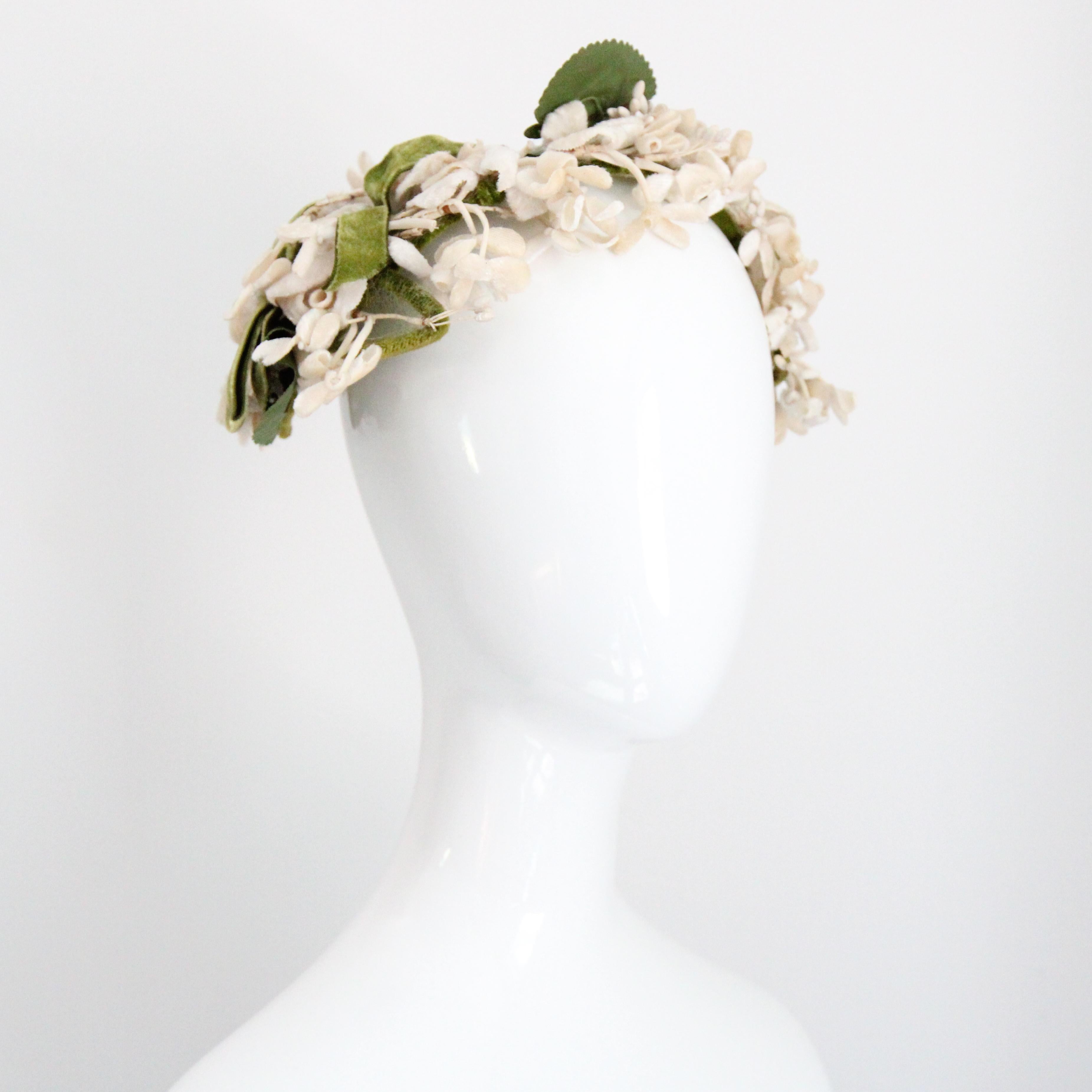 Dieser originelle Hut aus den 1950er Jahren ist in den prächtigsten Creme- und Grüntönen gehalten und mit Jasminblüten aus Samt verziert, die mit kleinen, verdrahteten Knospen und verstreuten grünen Blättern verziert sind. 

Die verdrahtete und