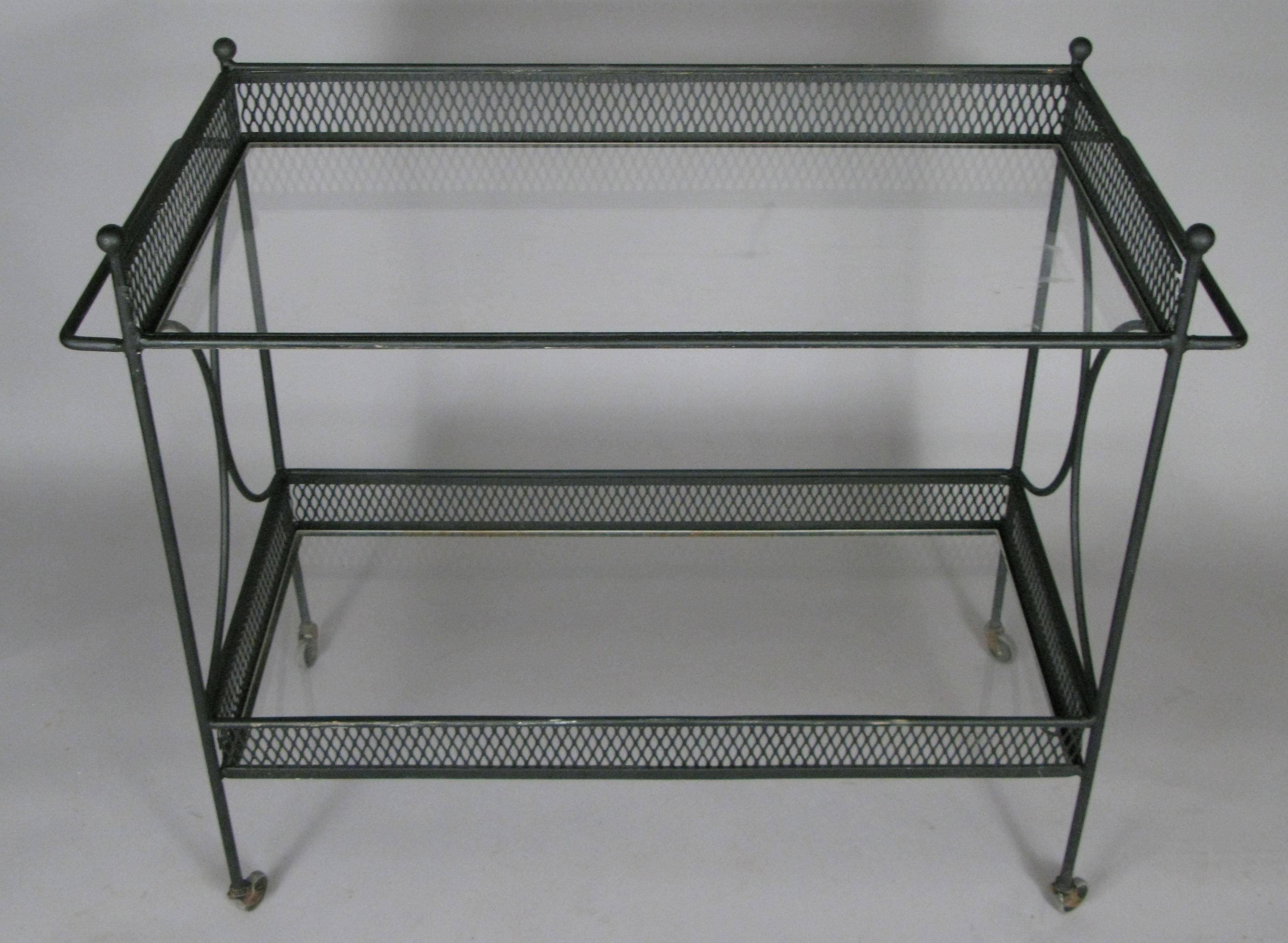 a classic modern wrought iron bar cart c. 1950 by Salterini. elegant large frame, with 2 full glass shelves, each with gallery rail. the sides have semi-circular design, and the corners have ball finials. 