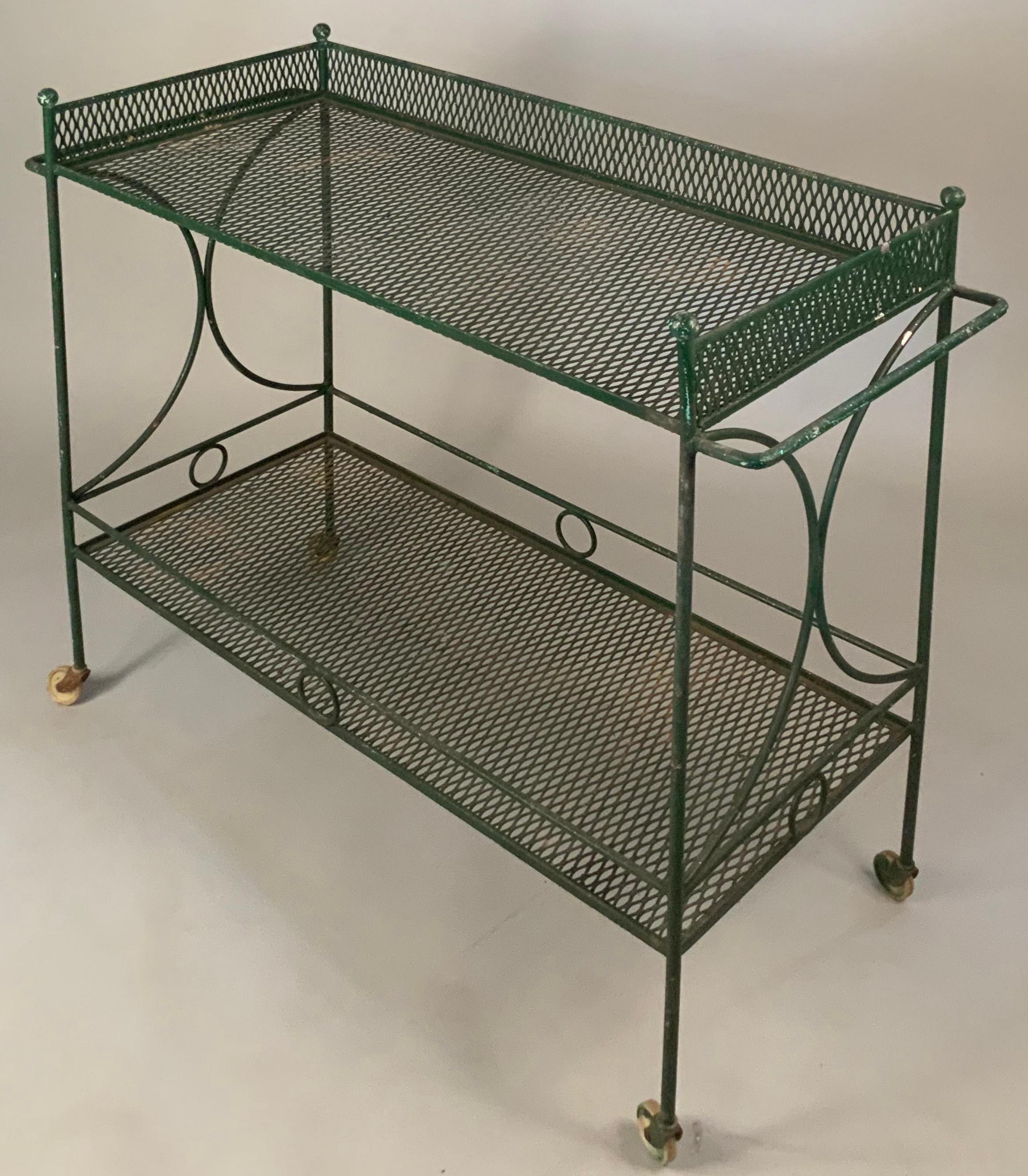 A classic modern wrought iron bar cart c. 1950 by Salterini. Elegant large frame, with 2 full expanded mesh shelves, which could have glass tops cut for them, each with gallery rail. The sides have semi-circular design, and the corners have ball