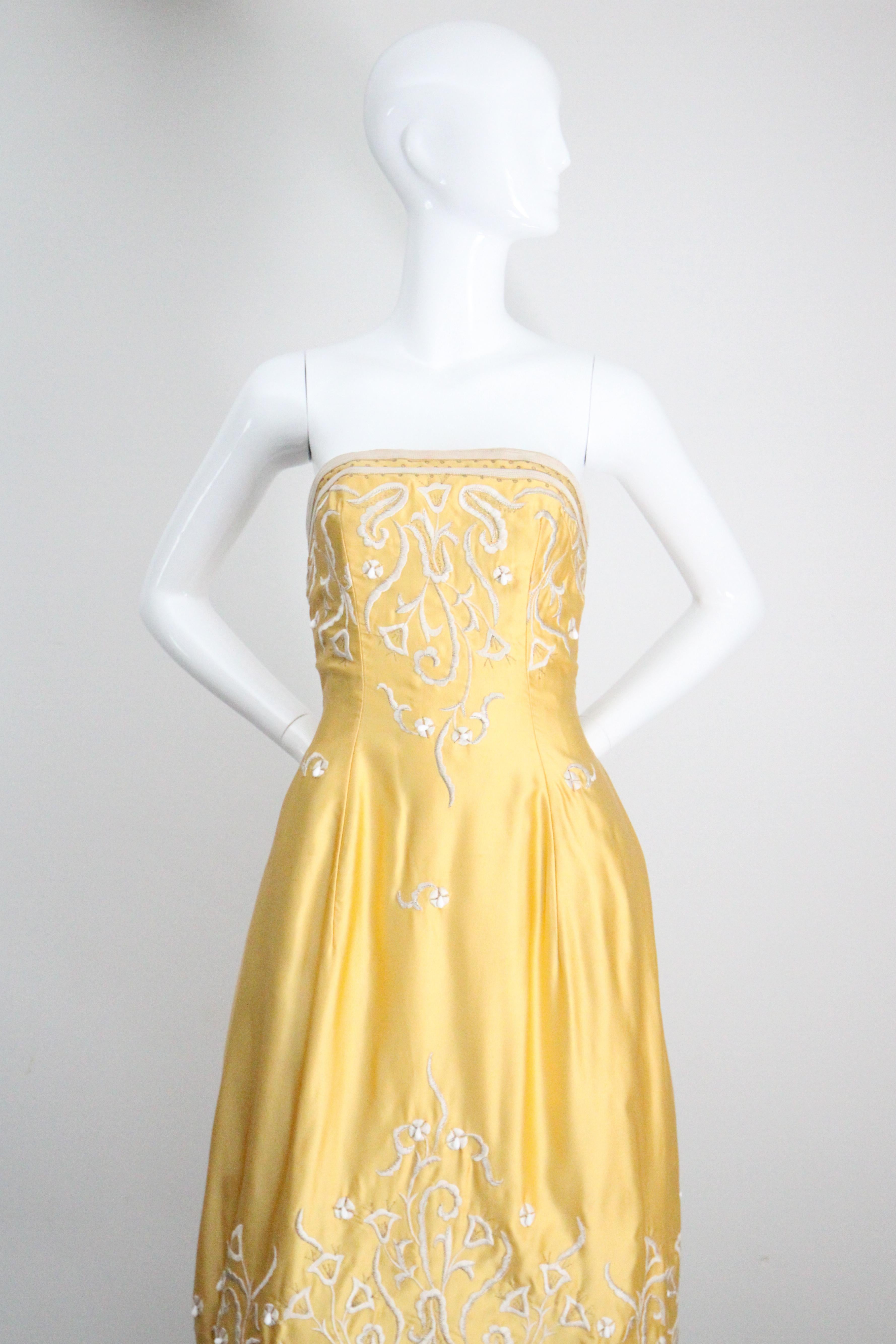 Cette époustouflante robe en satin jaune bouton d'or des années 1950, brodée d'un motif floral en fil de soie crème et rehaussée de perles de verre au lait, est la robe de cocktail parfaite pour votre garde-robe. 

Son encolure droite sans bretelles