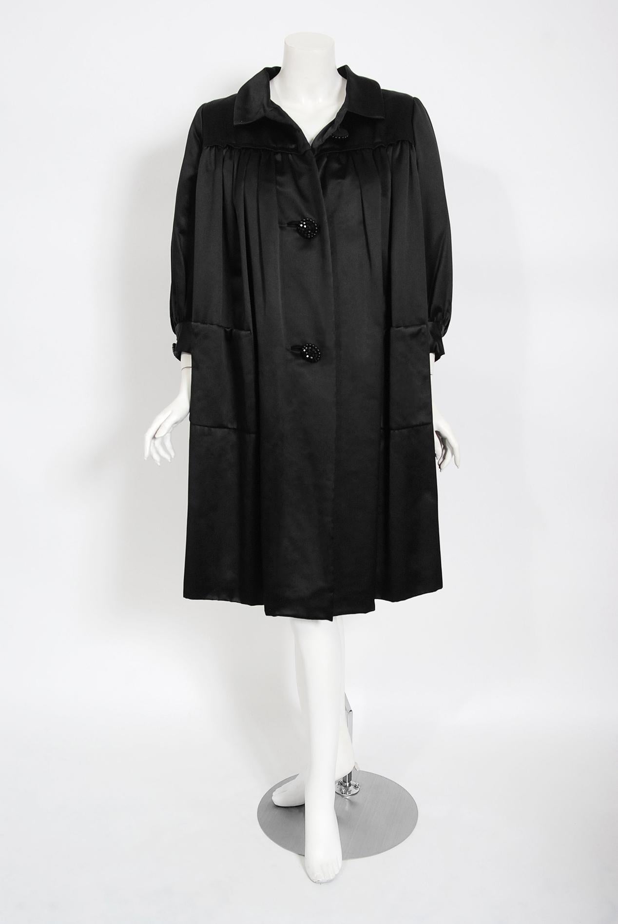 This exquisite Traina-Norell designer coat, fashioned in a high-quality duchess silk satin, exemplifies their signature blend of couture-level quality with quintessentially American style—elegant in its simplicity. This was a difficult piece to