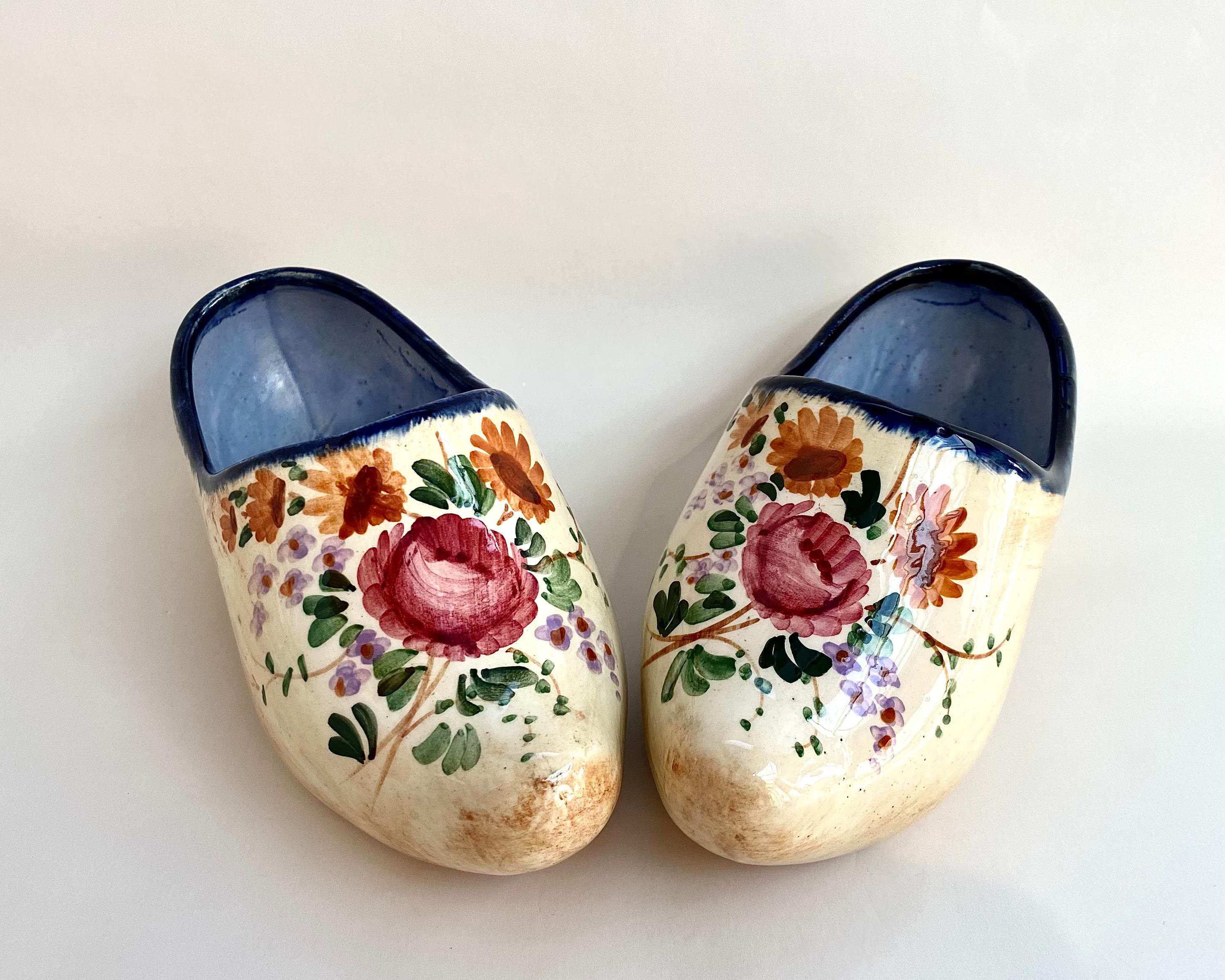 Une charmante paire de chaussures vintage créée sous la forme de sabots traditionnels.

Belgique, années 1960.

Les chaussures décoratives miniatures ont été fabriquées en porcelaine belge émaillée et présentent des motifs de fleurs et de feuilles