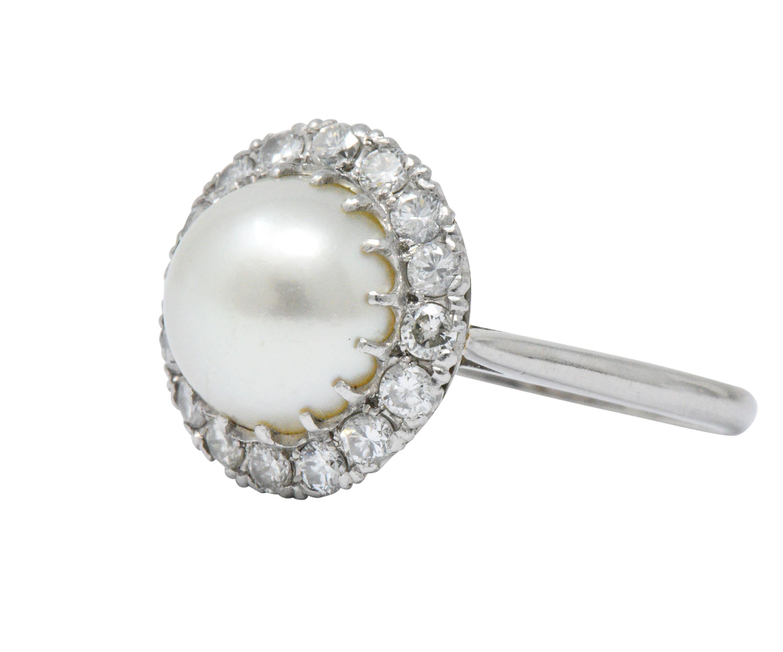 Centering a round cultured pearl, measuring approximately 9.6 mm, light cream body color with rose and green overtones, very good luster and surface quality 

Round brilliant cut diamond surround contains 16 diamonds weighing approximately 0.50