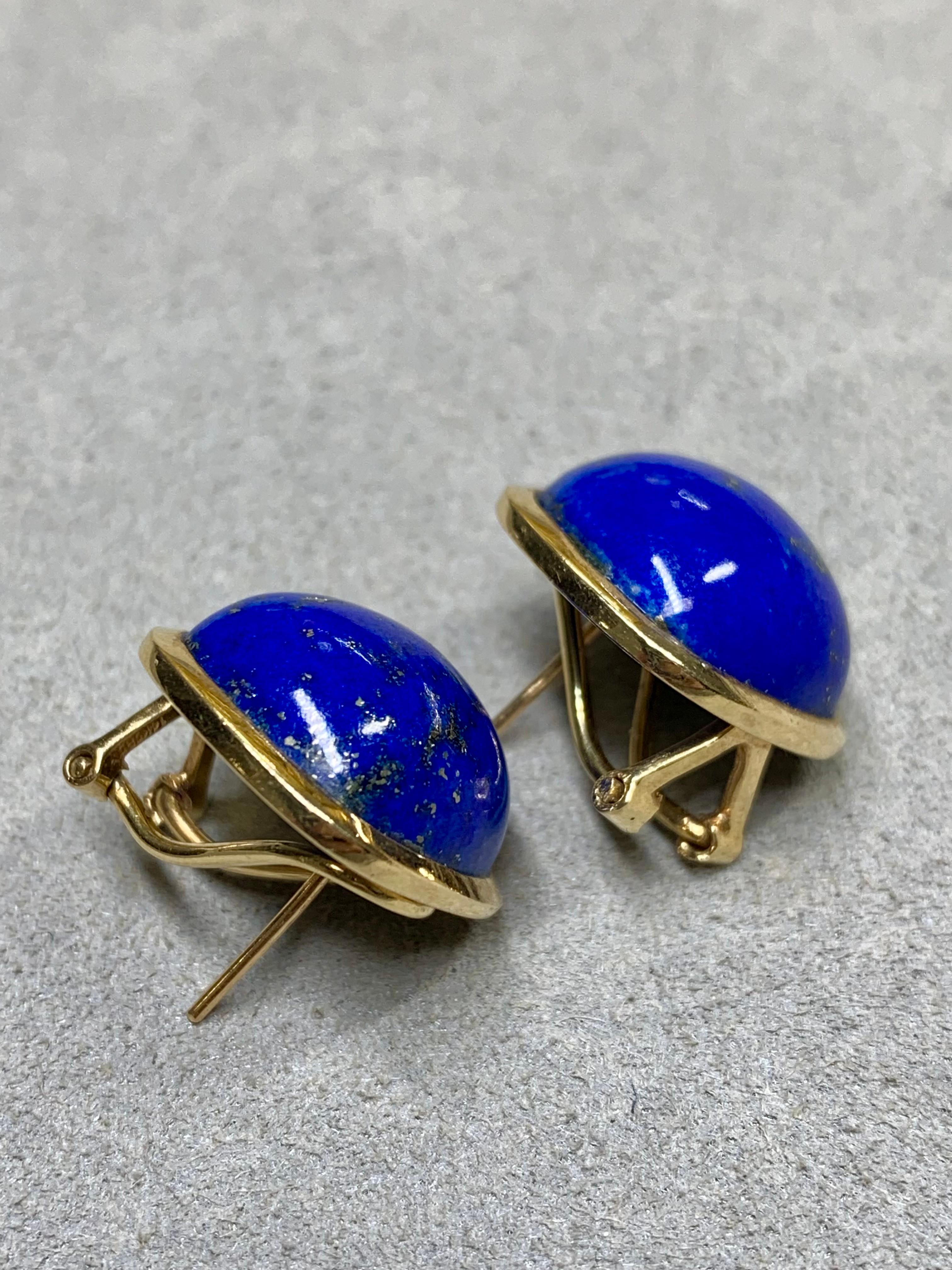 A classic pair of huggies circa the 1960s crafted in 14K yellow gold and set with cushion shaped cabochon natural lapis exhibiting beautiful patches of iron pyrite which add life and character to each stone. These earrings have posts with omega