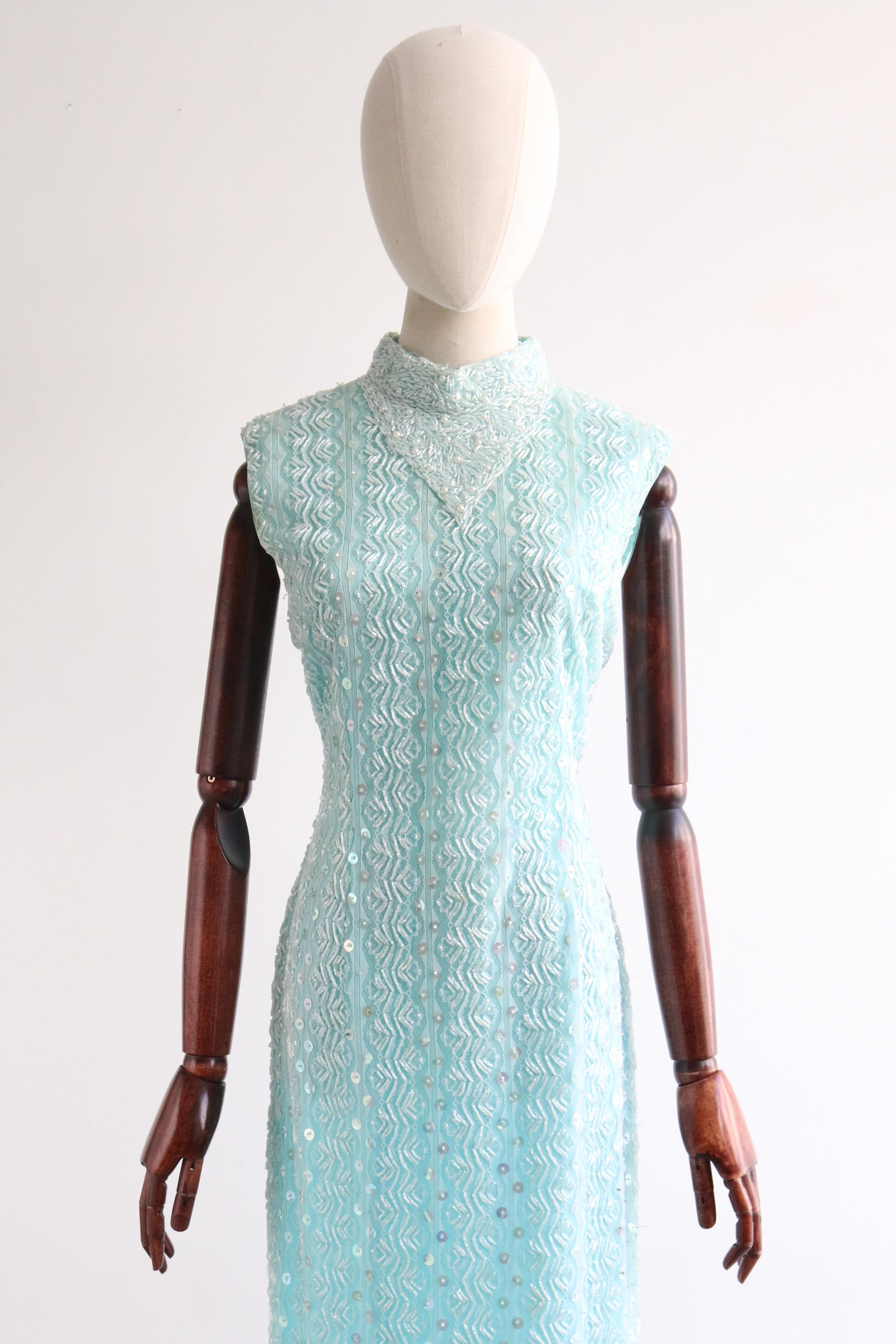 Dieses bezaubernde aquafarbene Kleid aus den 1960er Jahren ist mit einem hellblauen Überwurf aus floraler Spitze verziert, der wiederum mit perlmuttfarbenen Glasperlen, schillernden Pailletten und Perlen verziert ist - das perfekte Statement für