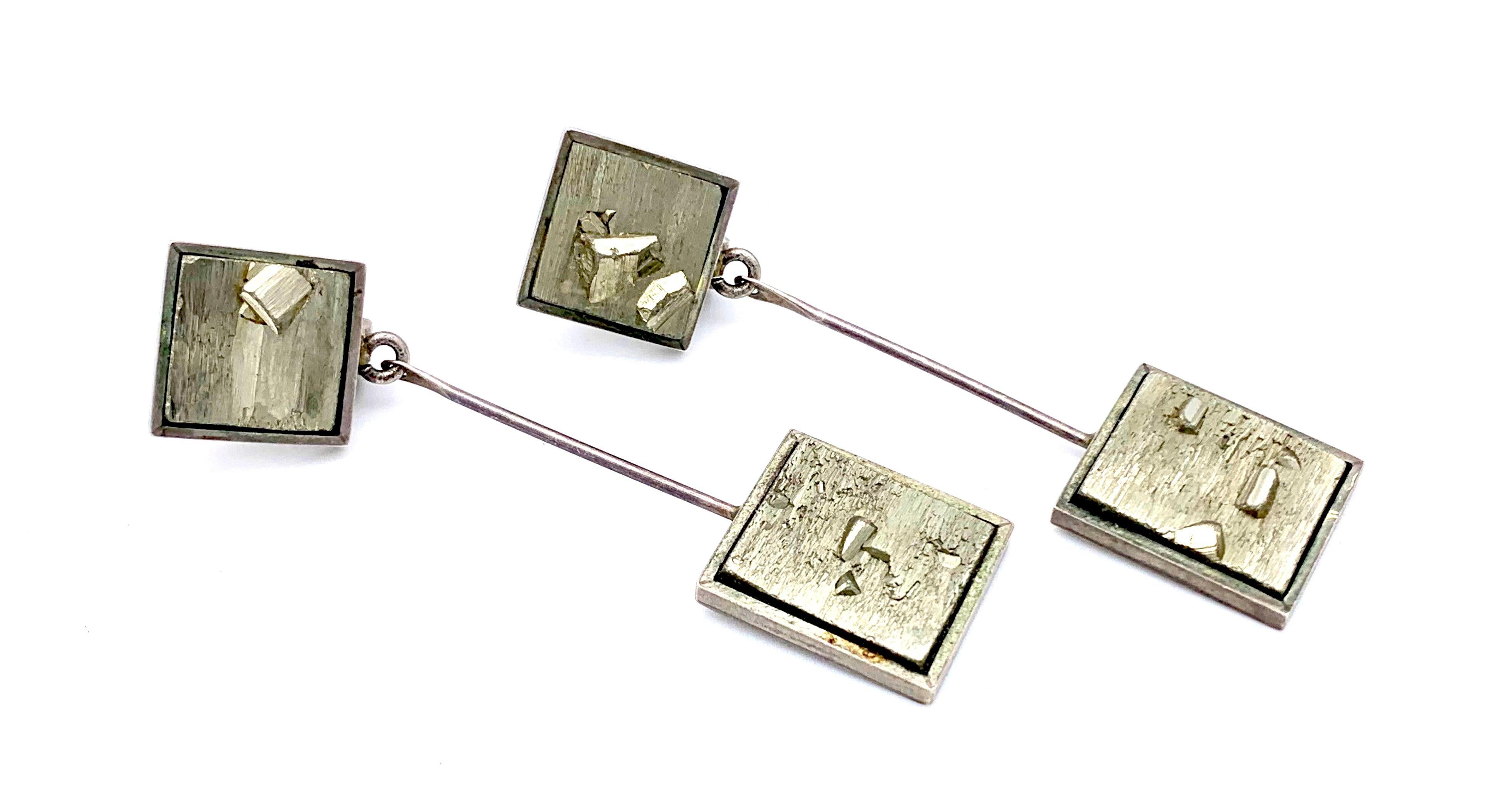 This elegant pair of  silver clip-on earrings was handcrafted in 1965 ca. The earrings are designed as  squares with the clip mechanisms on the reverse. The front of the ear clips are set with slices of pyrite. Suspended from each square is a