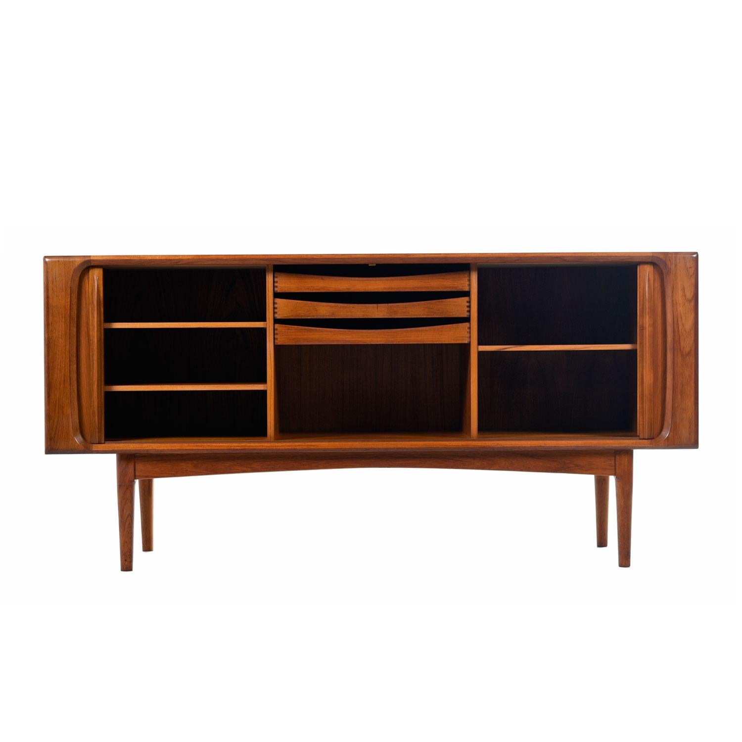 Vintage midcentury Scandinavian Modern Danish teak tambour door credenza by Bernhard Pedersen & Son. Expertly crafted with sleek lip-like, solid teak carved handles gracing the tambour doors. Open the cabinet to reveal cabinet space at left and