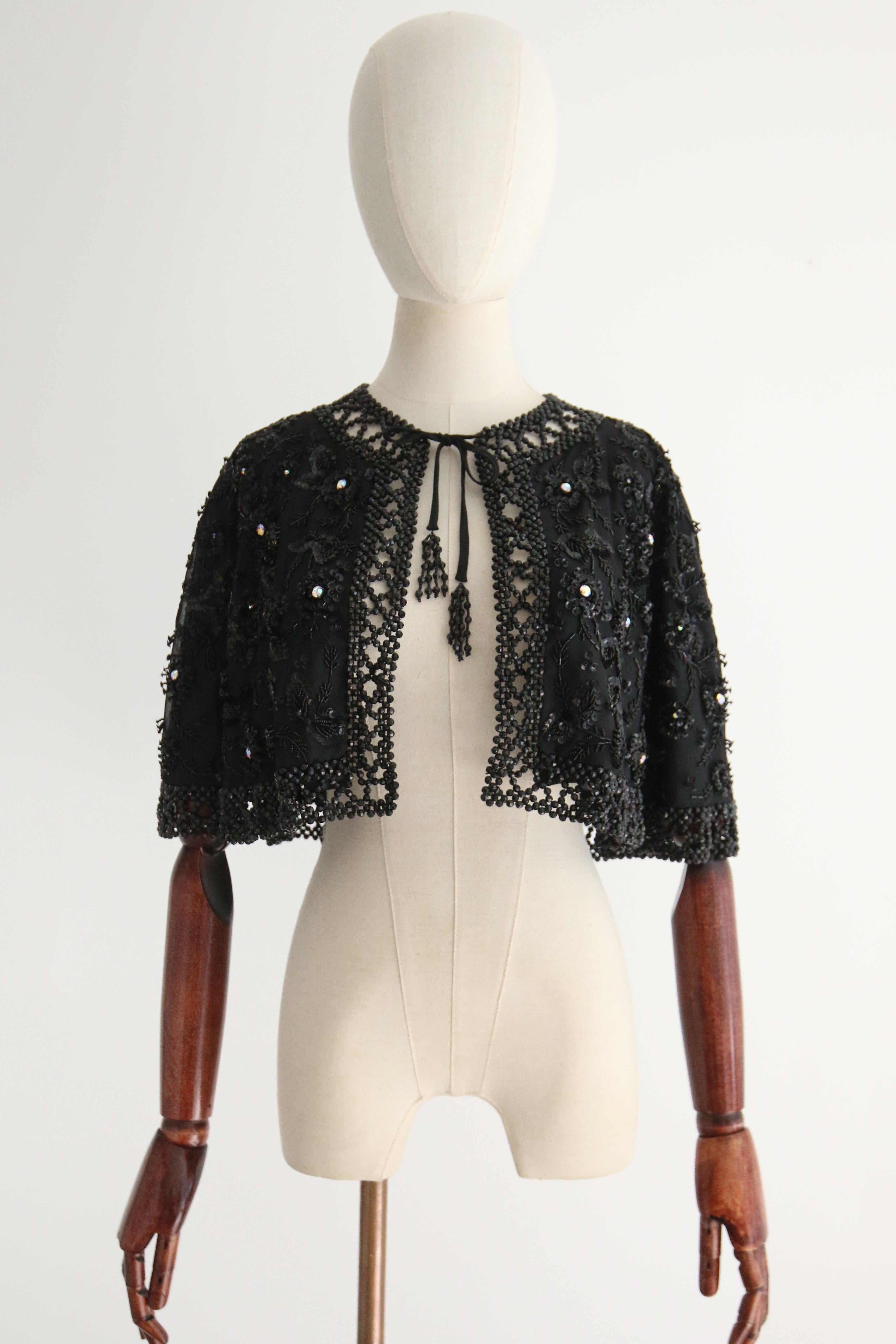 Dieses göttliche schwarze Schultercape aus den 1960er Jahren, das mit schwarzen Pailletten und Perlen verziert ist und mit großen, schillernden Strasssteinen in Krallenfassung in einem floralen Muster akzentuiert ist, ist der perfekte Abschluss