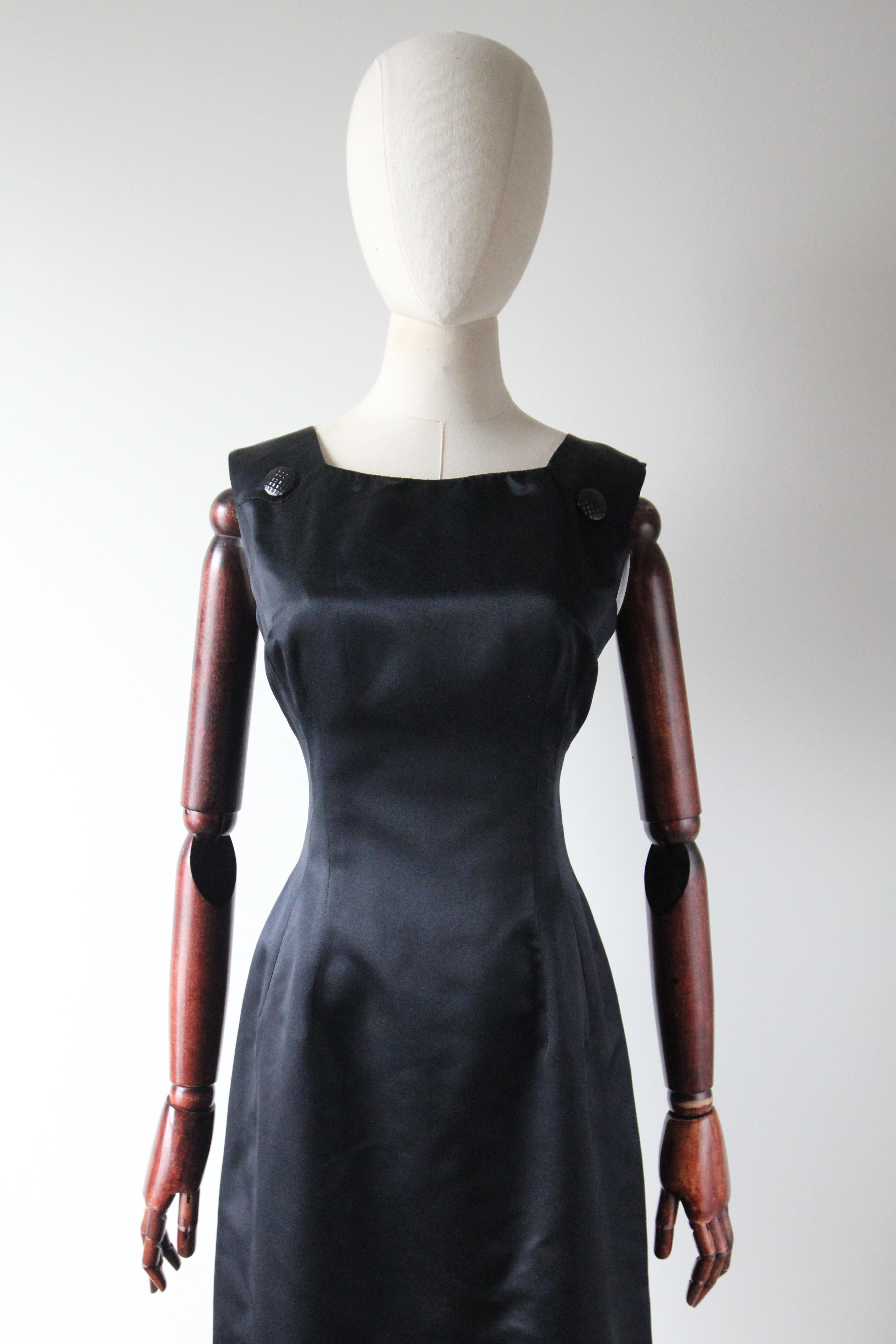 Realizzato alla perfezione, questo abito Anne Fogarty in raso nero dei primi anni '60 è il numero perfetto da aggiungere al tuo guardaroba da cocktail.  
La scollatura arrotondata è incorniciata da spalline larghe, che si uniscono a ciascun lato del
