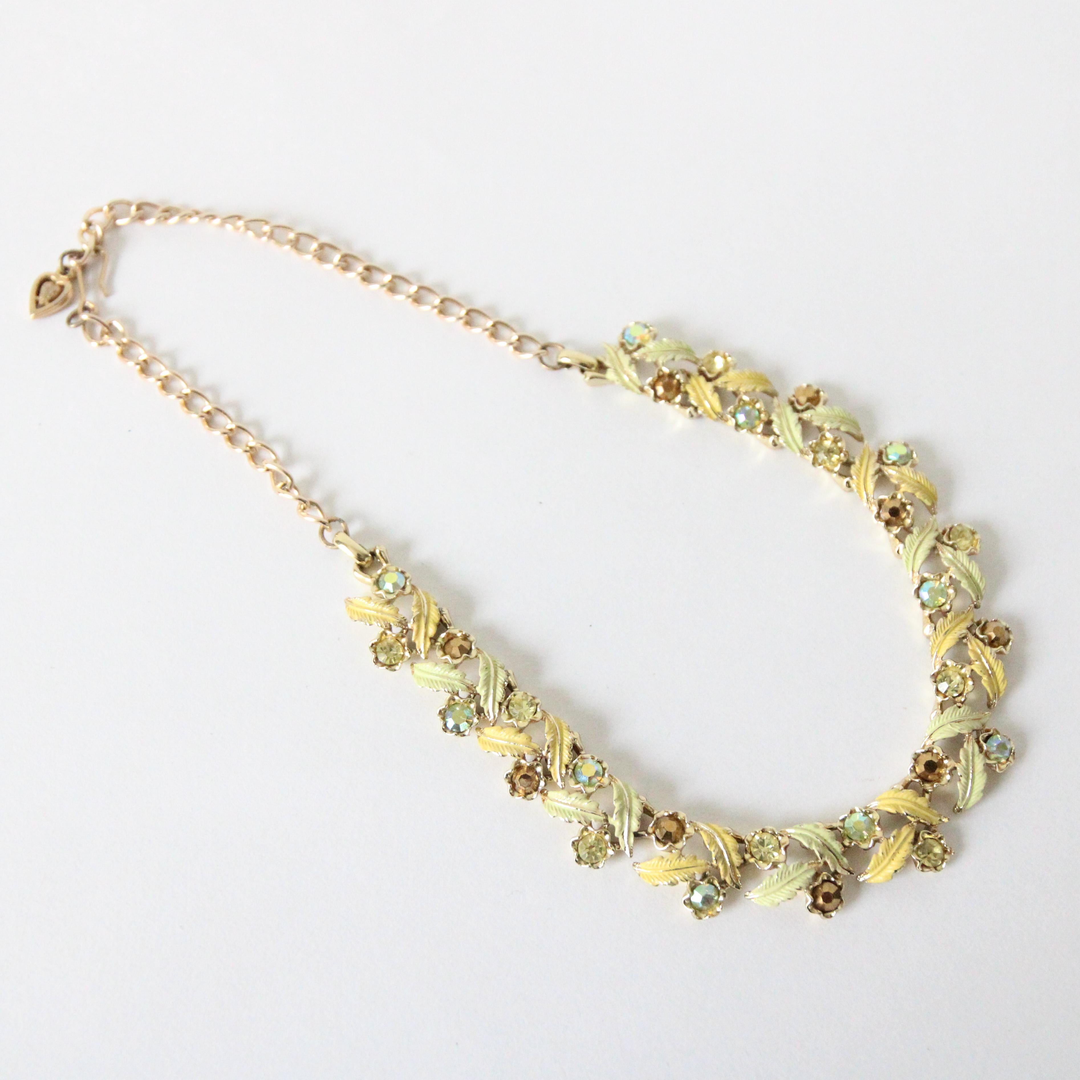 Una bellezza da vedere, questa originale collana dipinta con strass e smalto degli anni '60, accentuata da strass intarsiati verdi, bronzo e chartreuse iridescente, che sono racchiusi in forme floreali in tonalità oro, circondate da foglie curve