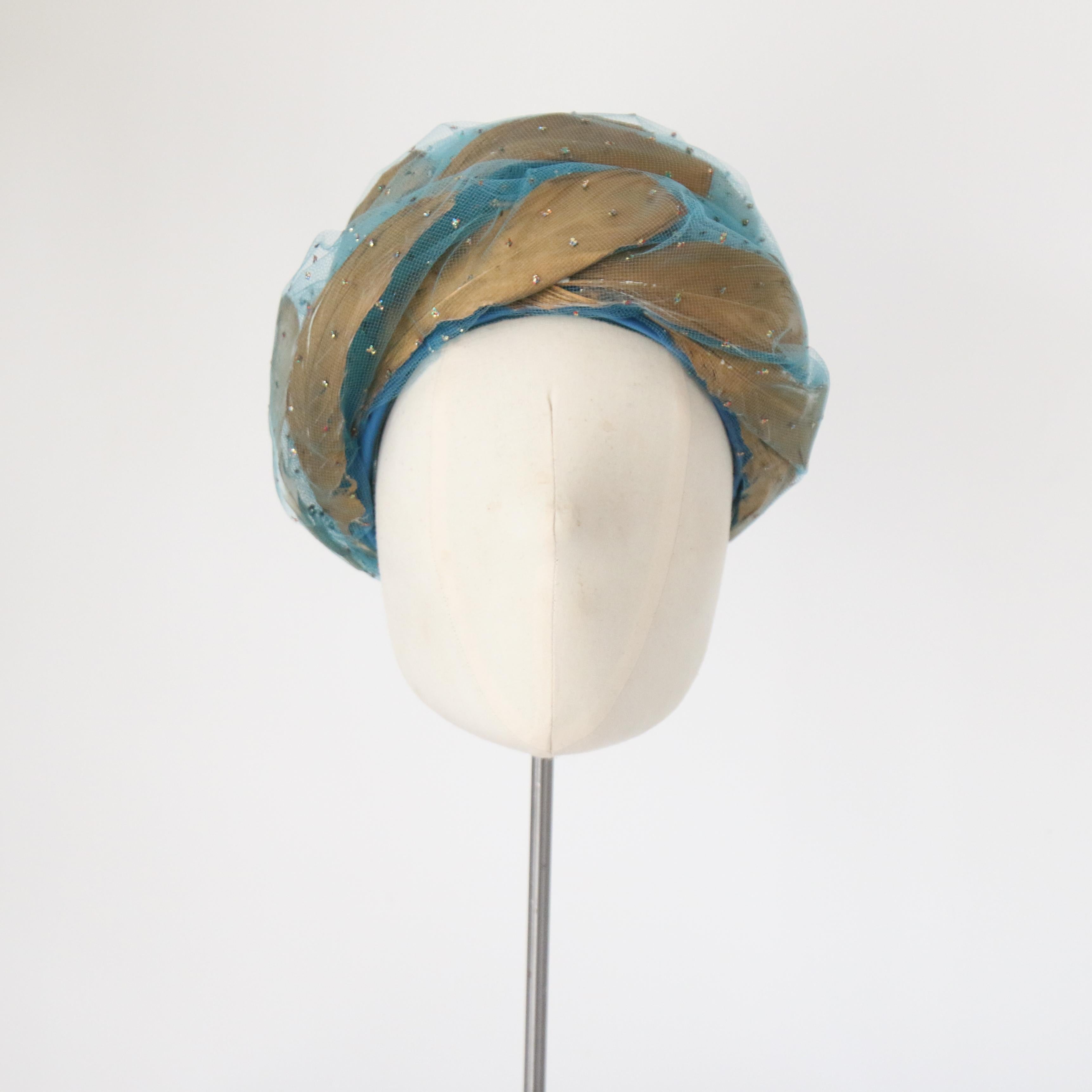 Cet époustouflant turban en tulle turquoise de Christian Dior, datant des années 1960, présente un design structurel en spirale avec des plumes métalliques dorées entrelacées et des points de paillettes multicolores irisées. Il s'agit d'une pièce