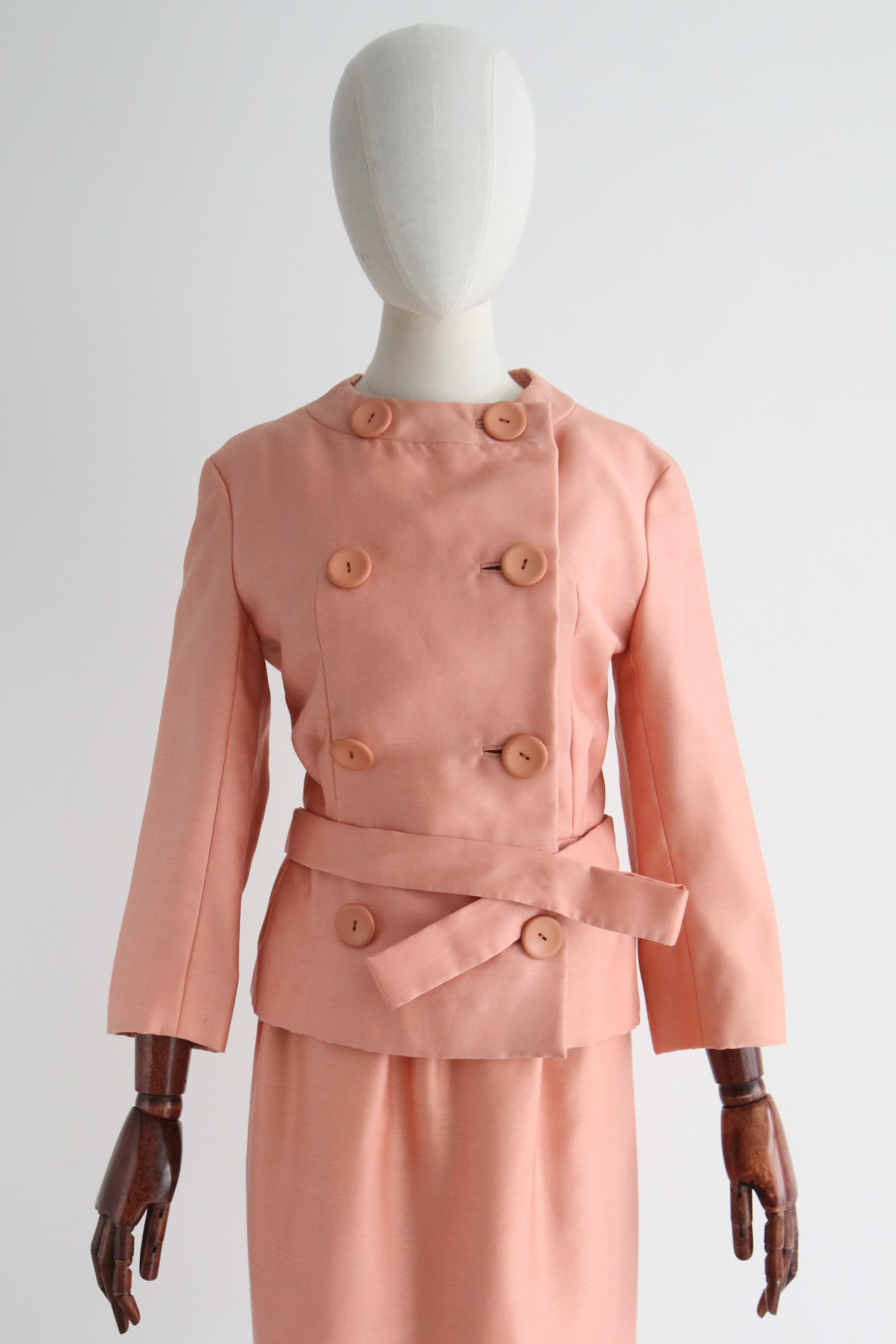 Réalisée dans la plus élégante nuance de soie pêche, cette combinaison jupe originale de Christian Dior des années 1960 est un ajout rare à votre collection vintage. 

L'encolure arrondie de la veste est encadrée par un col à panneaux qui se