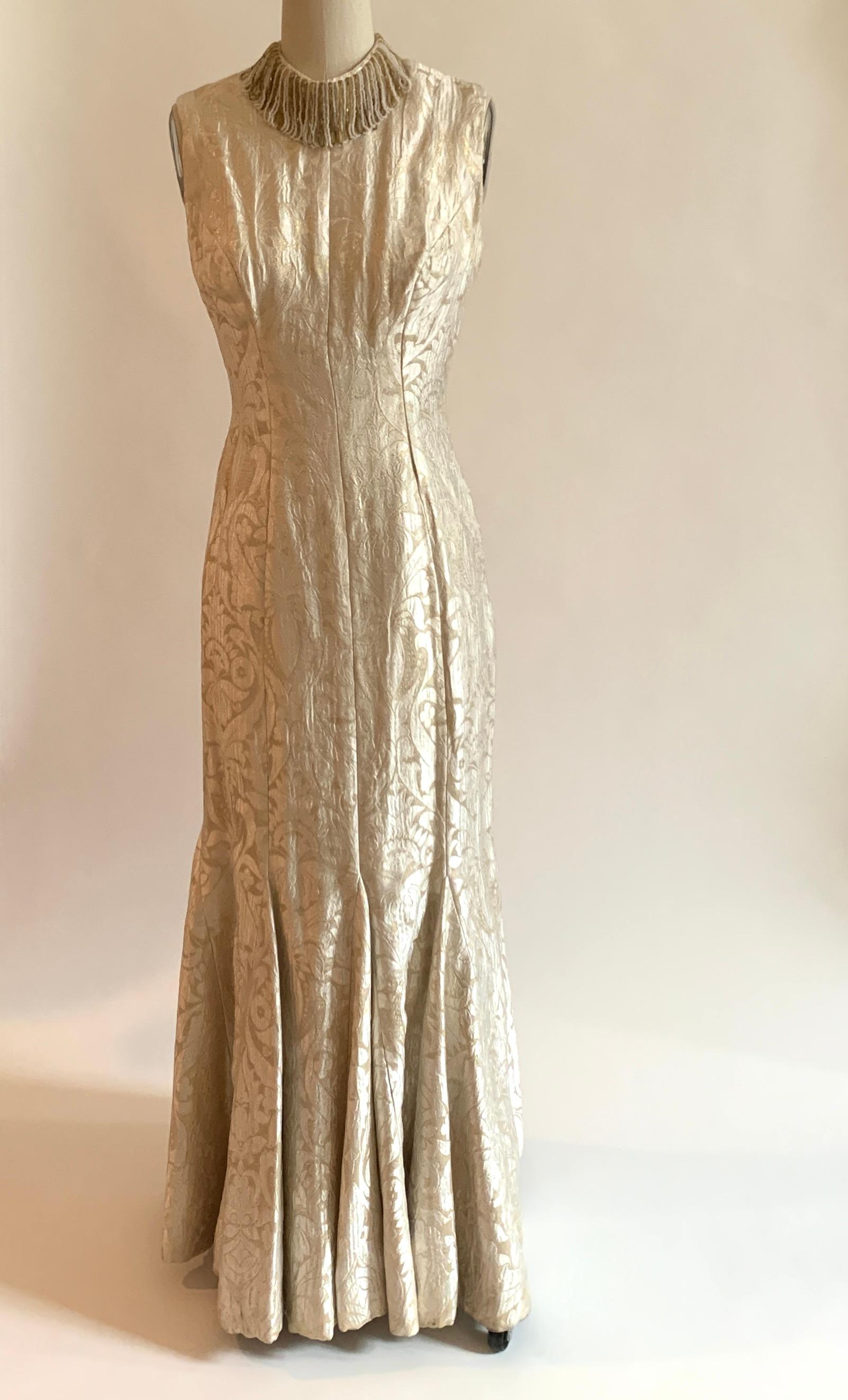 Stunning vintage 1960s sleeveless fluted gown and coat set set in cream and pale gold brocade. Gown has a beautiful fit and flare shape with a deep scoop back and beading at neck. Lined in silky material. 

Coat features mid length sleeves , a