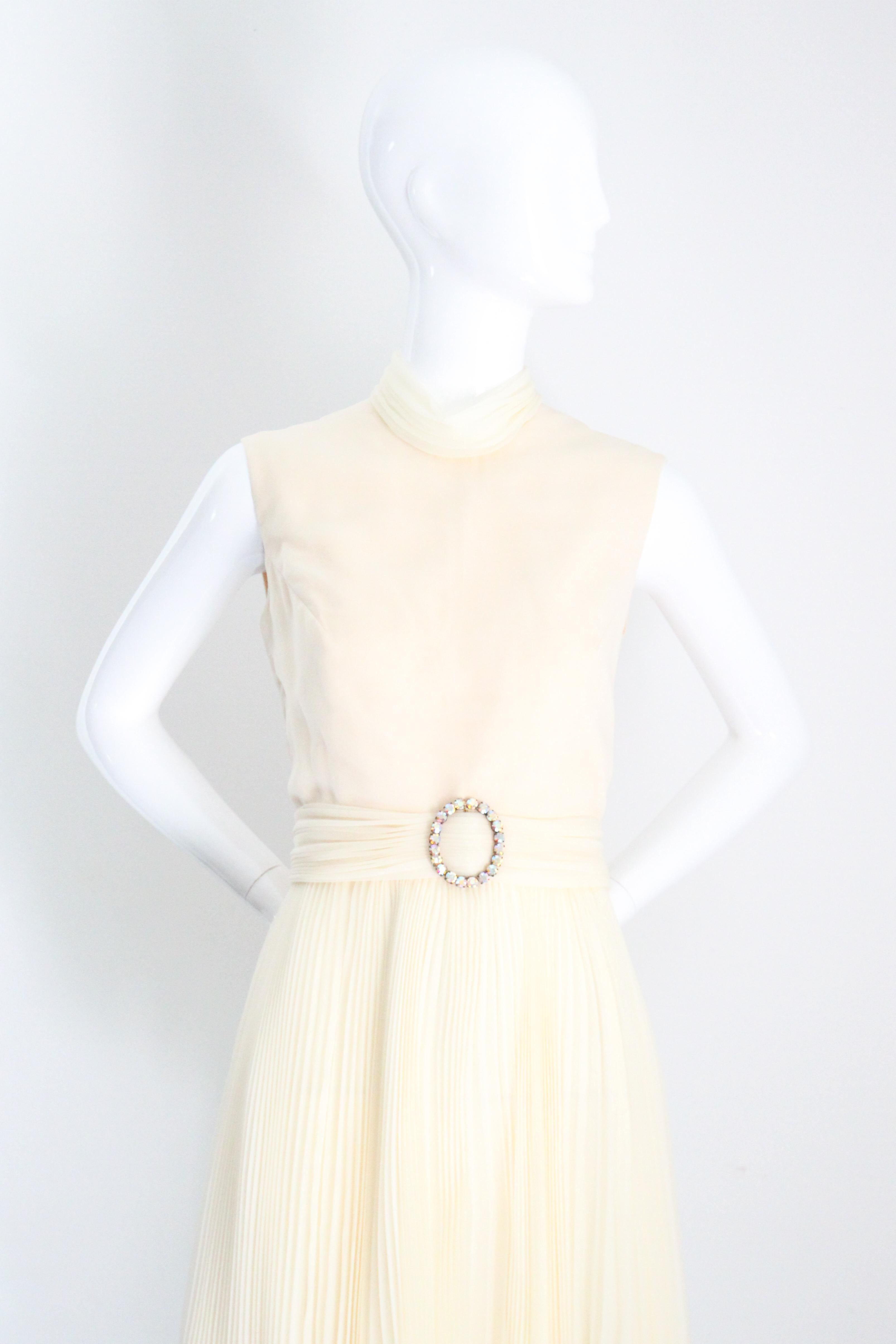 Dieses originelle Faltenkleid aus den 1960er Jahren ist in einem zarten cremefarbenen Chiffon gehalten und mit schillernden Strasssteinen besetzt,  ist genau das richtige Stück, um Ihre Vintage-Sammlung zu ergänzen.

Der runde Halsausschnitt wird