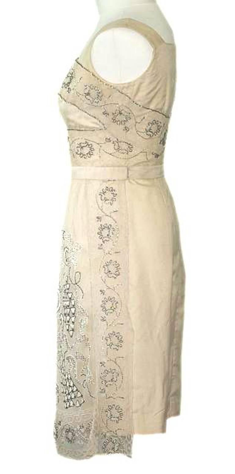 This cream silk dress is embellished with beautiful hand made lace. Circa 1960s. It is fully lined with white acetate. 
There is a zip at the back with a hook at the top and underarm dress shields to protect the garment from perspiration.
The