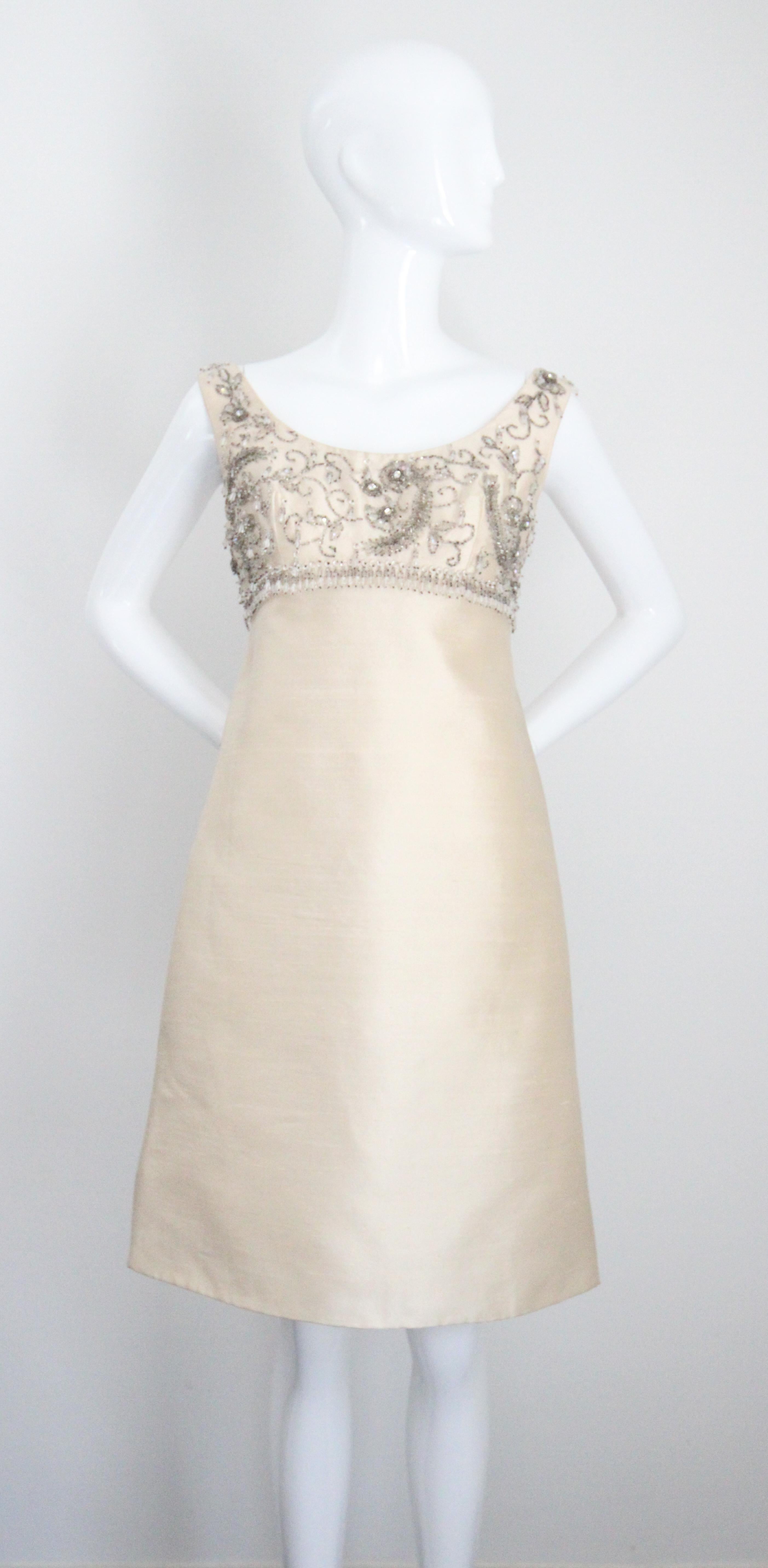  Este majestuoso conjunto de vestido y abrigo de shantung de seda color crema de los años 60, adornado con cuentas de cristal plateadas, brillantes plateados y gotas de cristal transparente facetado, es la pieza perfecta para esa ocasión especial. 