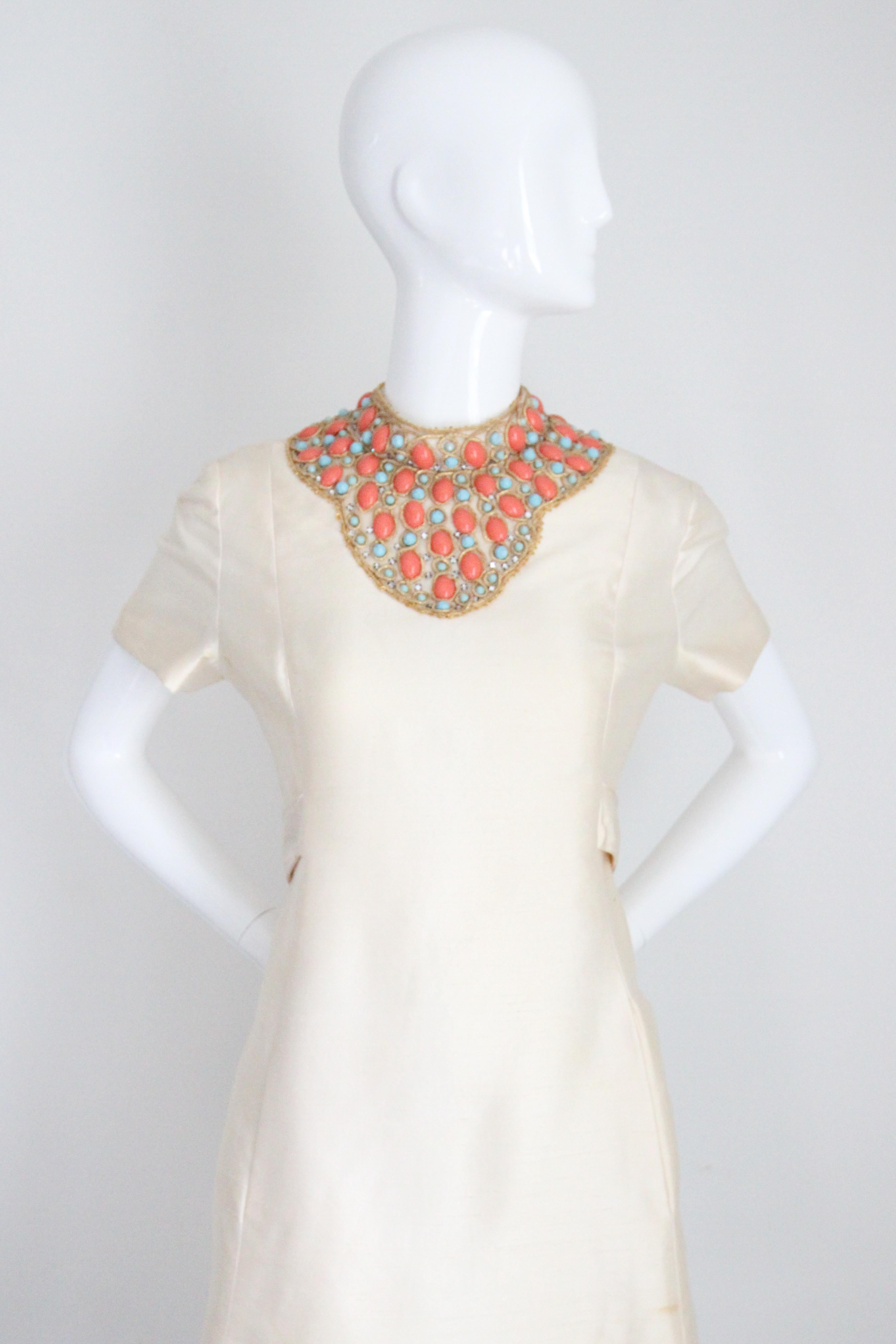 Dieses originelle, cremefarbene Shantung-Seidenkleid aus den 1960er Jahren ist ein echter Blickfang. Es ist mit türkis- und korallenfarbenen Cabochons und goldenen Soutache-Stickereien verziert und genau das Richtige für Ihre Cocktailgarderobe. 
