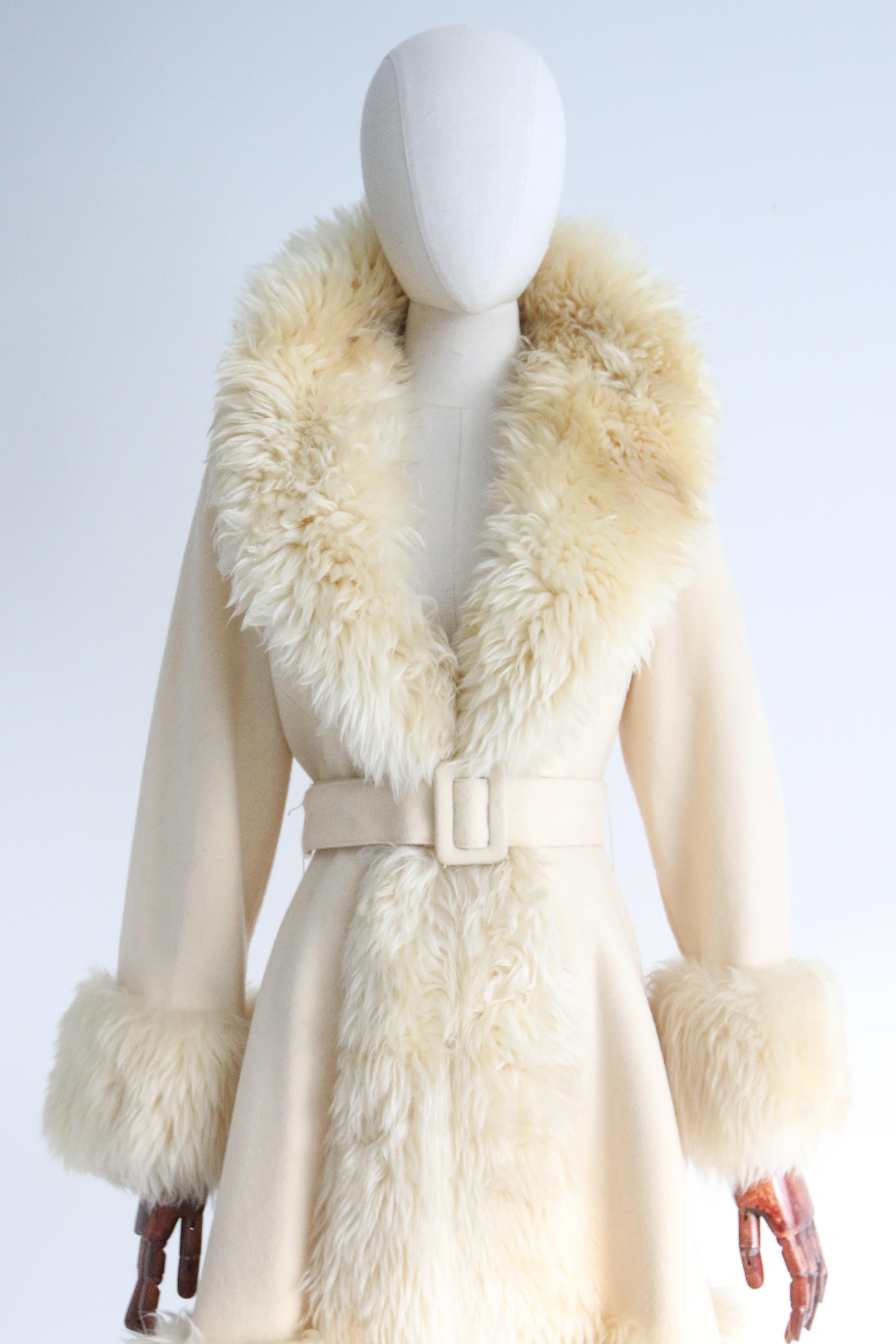 An iconic piece of fashion, this original 1960's cream wool coat with faux sheepskin accents is the perfect piece to welcome the cooler months with. 
The deep v shaped neckline is edged with a wide faux sheepskin collar, drawing in along the front