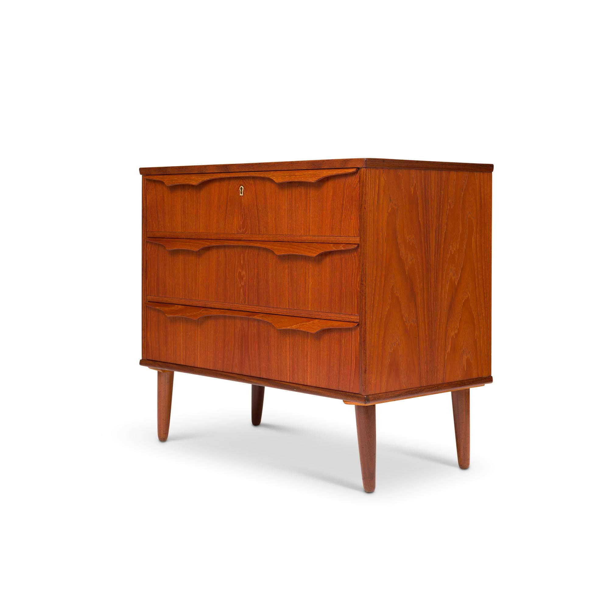 
Exuding timeless elegance, this vintage Danish mid-century modern lowboy dresser boasts exquisite teak wood grain that captivates the eye. Its allure lies in the three impeccably crafted drawers adorned with intricately carved drawer pulls, all in