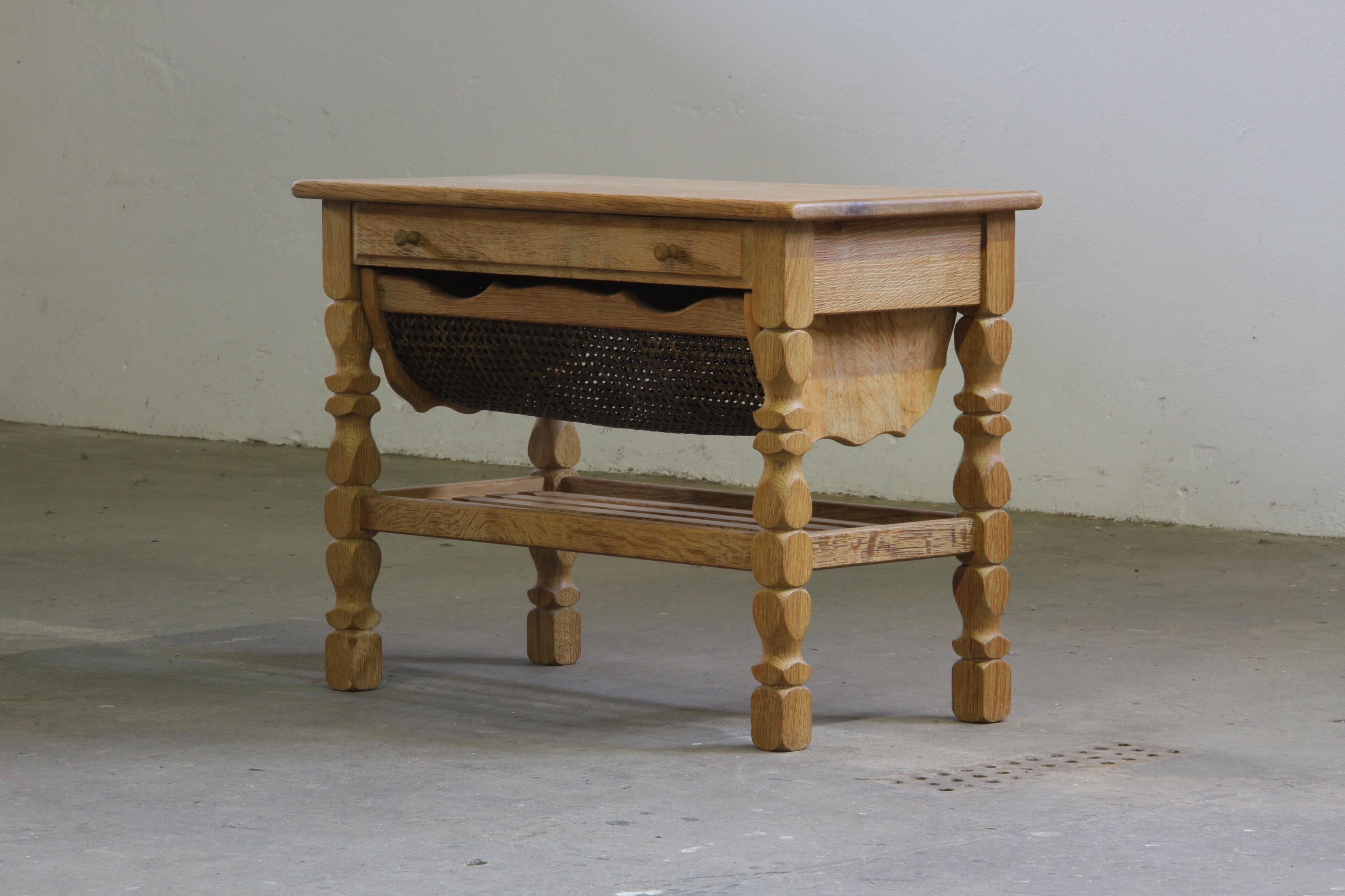 This Danish sewing table, crafted in the 1960s from solid oak, showcases great craftsmanship. Featuring a drawer with storage and an extendable wicker basket, it adapts to various uses. 

The legs draw inspiration from Henning Kjærnulf's design