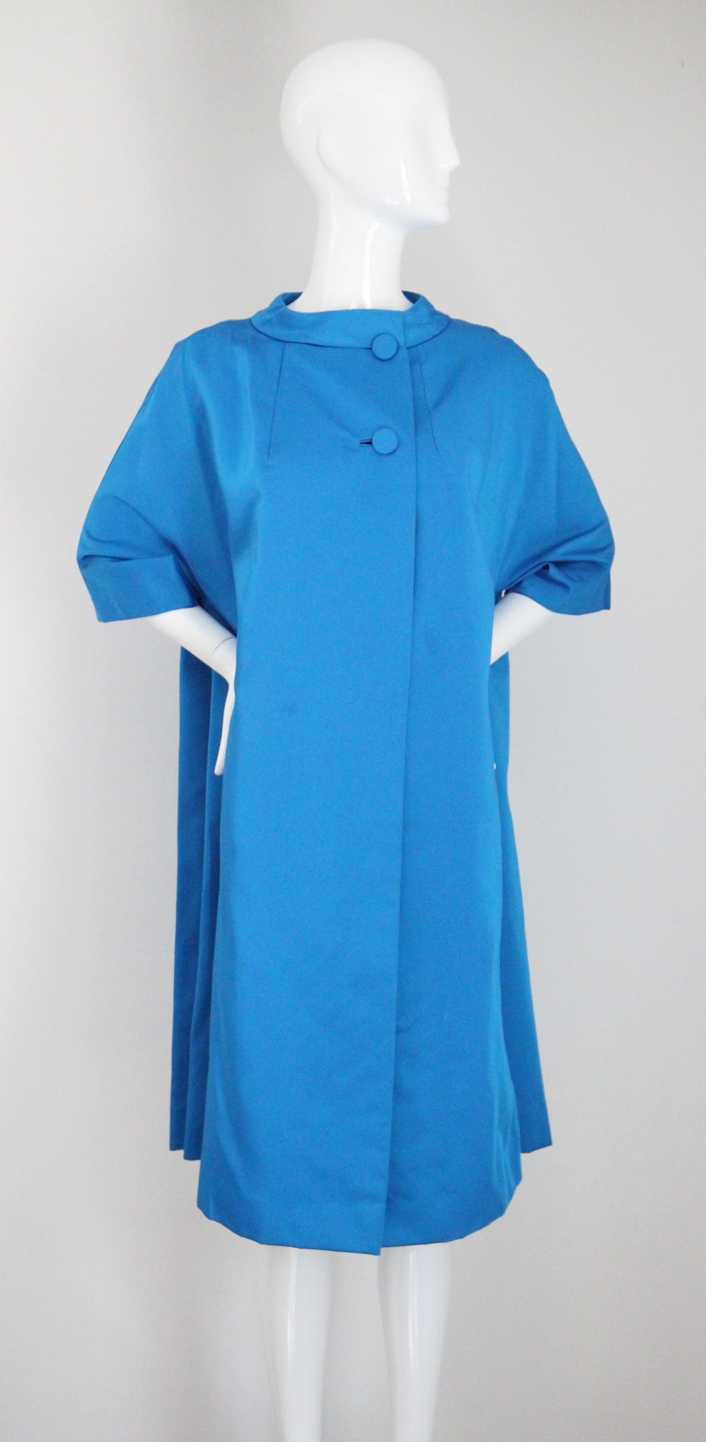 Este abrigo original de Neiman Marcus de los años 60, en el tono más vibrante de satén azul cobalto eléctrico, es la pieza perfecta para añadir a tu colección vintage.

El cuello redondeado y levantado de estilo mandarín, se une a lo largo del lado