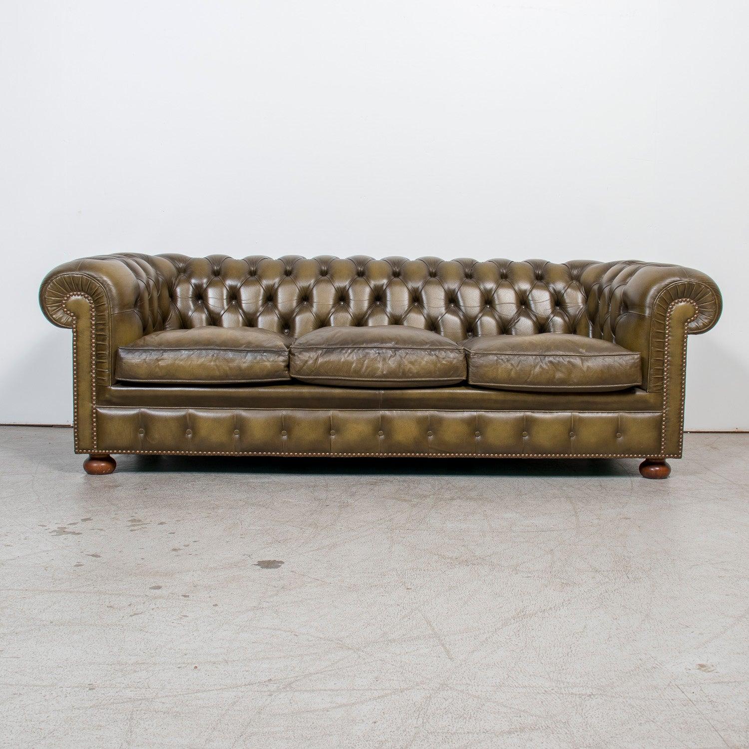 A striking vintage English Chesterfield sofa in rich olive green leather, crafted in the Victorian style during the mid-20th century, circa 1960s. This iconic three-seat sofa captures all the hallmarks of traditional Chesterfield design: a fully