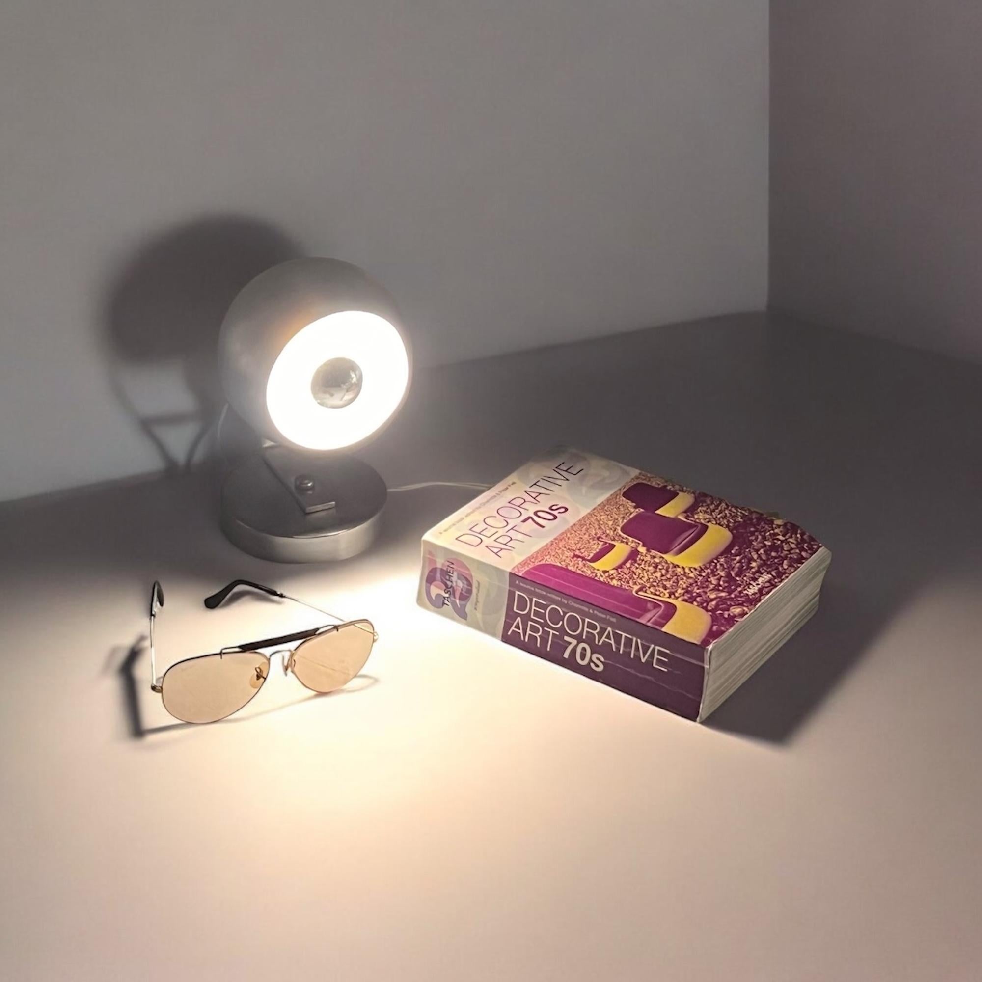 This 1960s Italian Eyeball lamp exemplifies high-quality mid-century design. Constructed from lightweight aluminum, it offers both durability and visual appeal. The lamp features its original wiring and accommodates an E14 bulb. For those seeking
