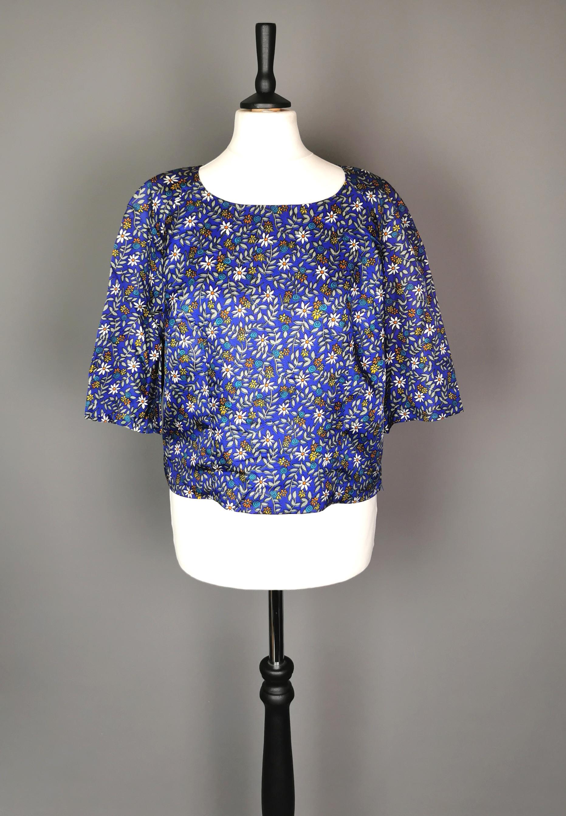 Eine wunderschöne Flower-Power-Bluse aus den 1960er Jahren.

Es ist kurz und leicht tailliert geschnitten, hat kurze Ärmel und einen runden Rundhalsausschnitt.

Die Bluse hat einen dunklen kobaltblauen Grund mit einem floralen Allover-Druck.

Es ist