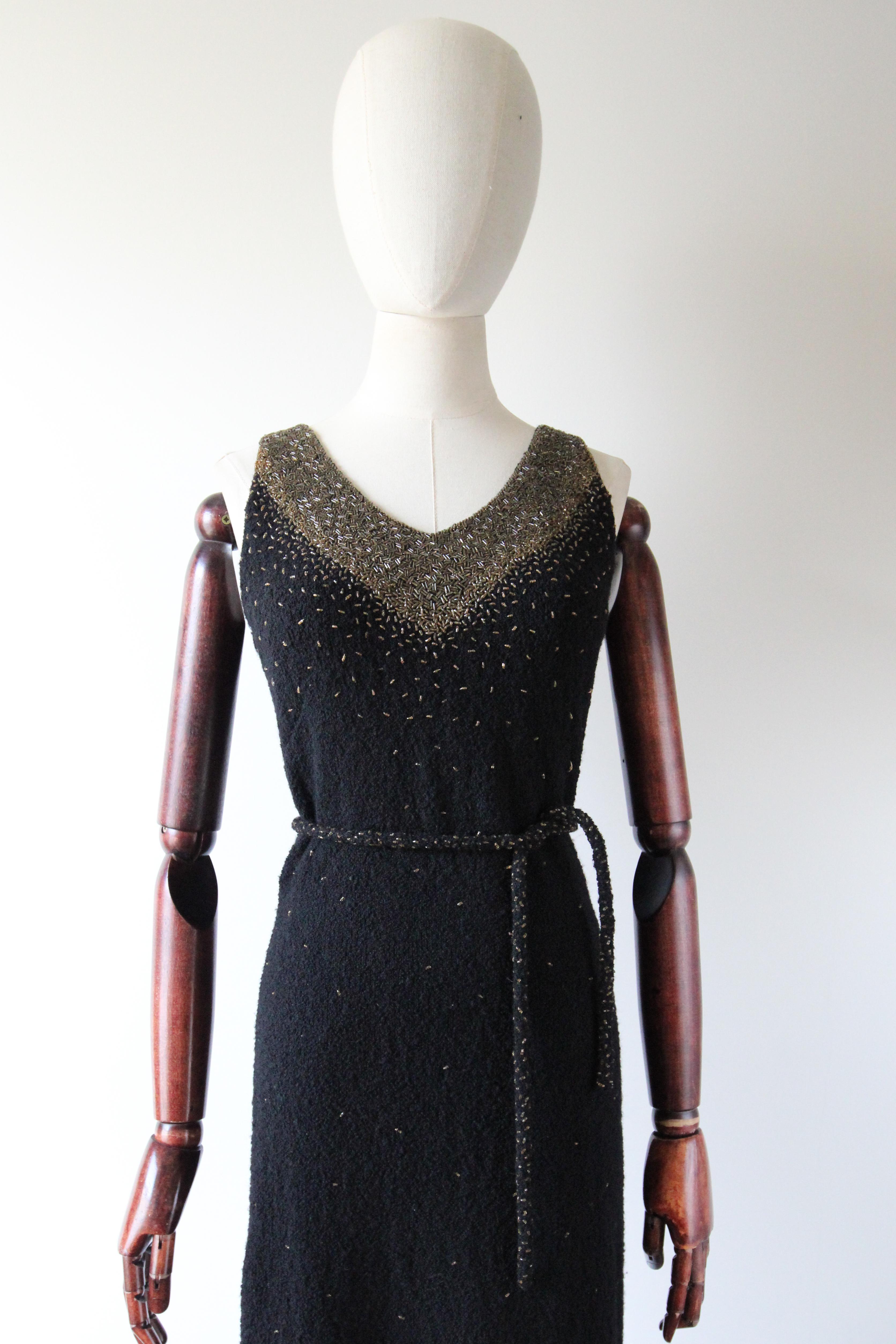 A classic silhouette rendered in a mesmerising design, this original 1960's Gene Shelly black wool evening dress, embellished with gold glass beadwork, is a timeless classic. 

The V shaped neckline is framed by medium width shoulder straps, which