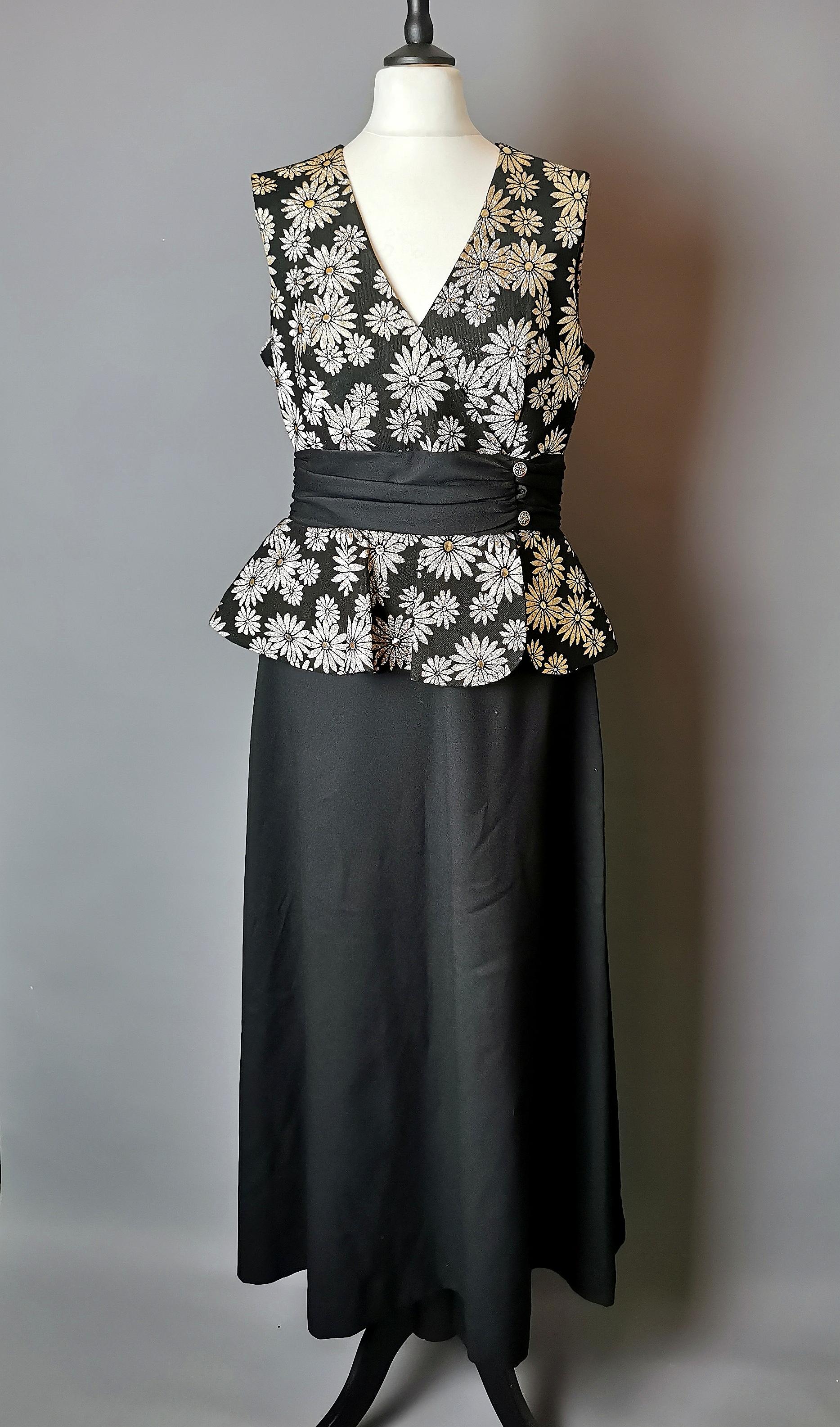 A gorgeous vintage 1960s Gold and silver floral Brocade dress.

A figure hugging dress with a pencil silhouette in black with a gold and silver brocade bodice with a sash and peplum waist.

It is made from a synthetic fabrics including polyester and