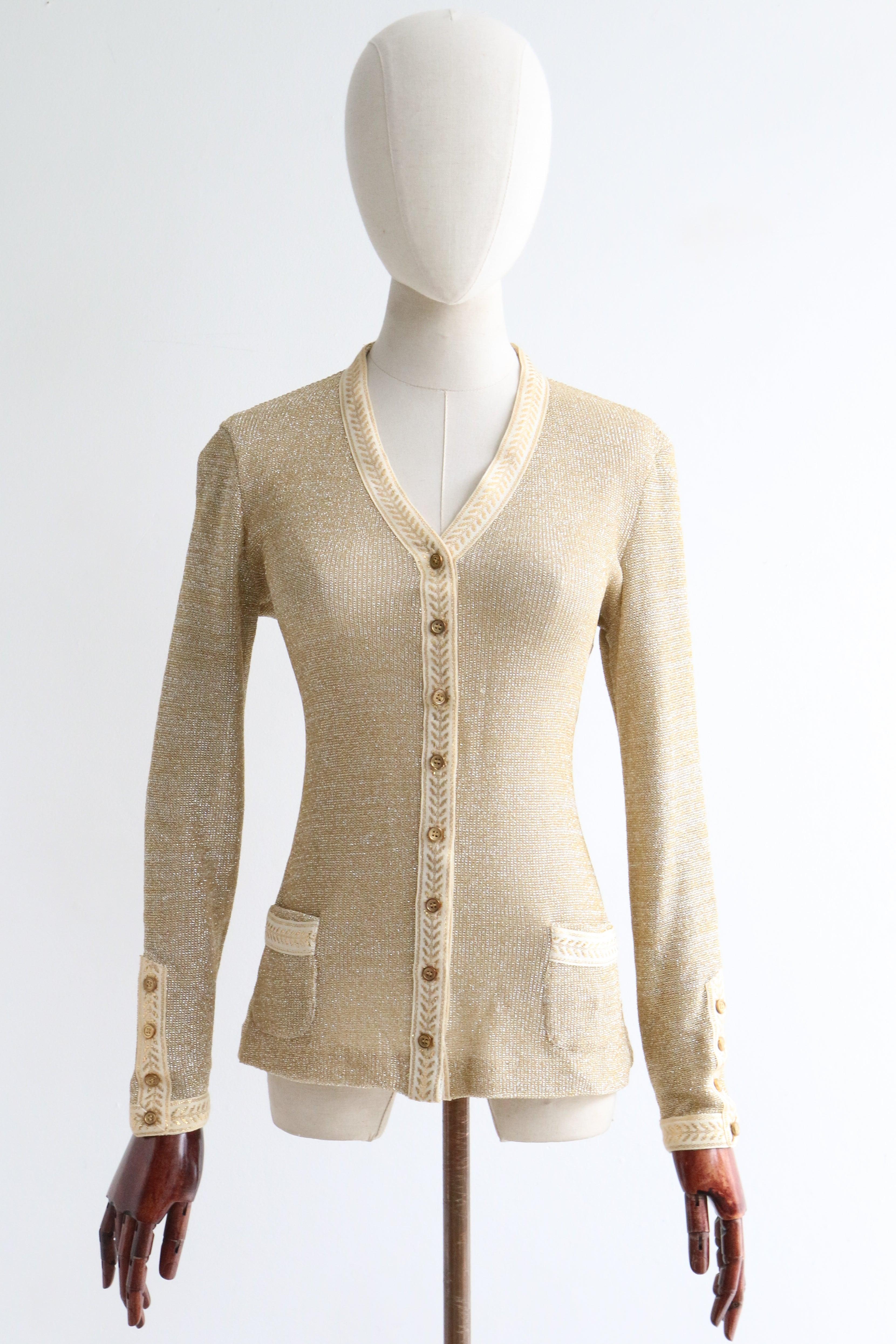 This sparkling 1960's gold knitted lurex cardigan, decorated with cream and gold embroidered ribbon with a laurel leaf design, is the perfect touch of sparkle to add to your everyday wardrobe. 

The V shaped neckline of the cardigan is framed by a