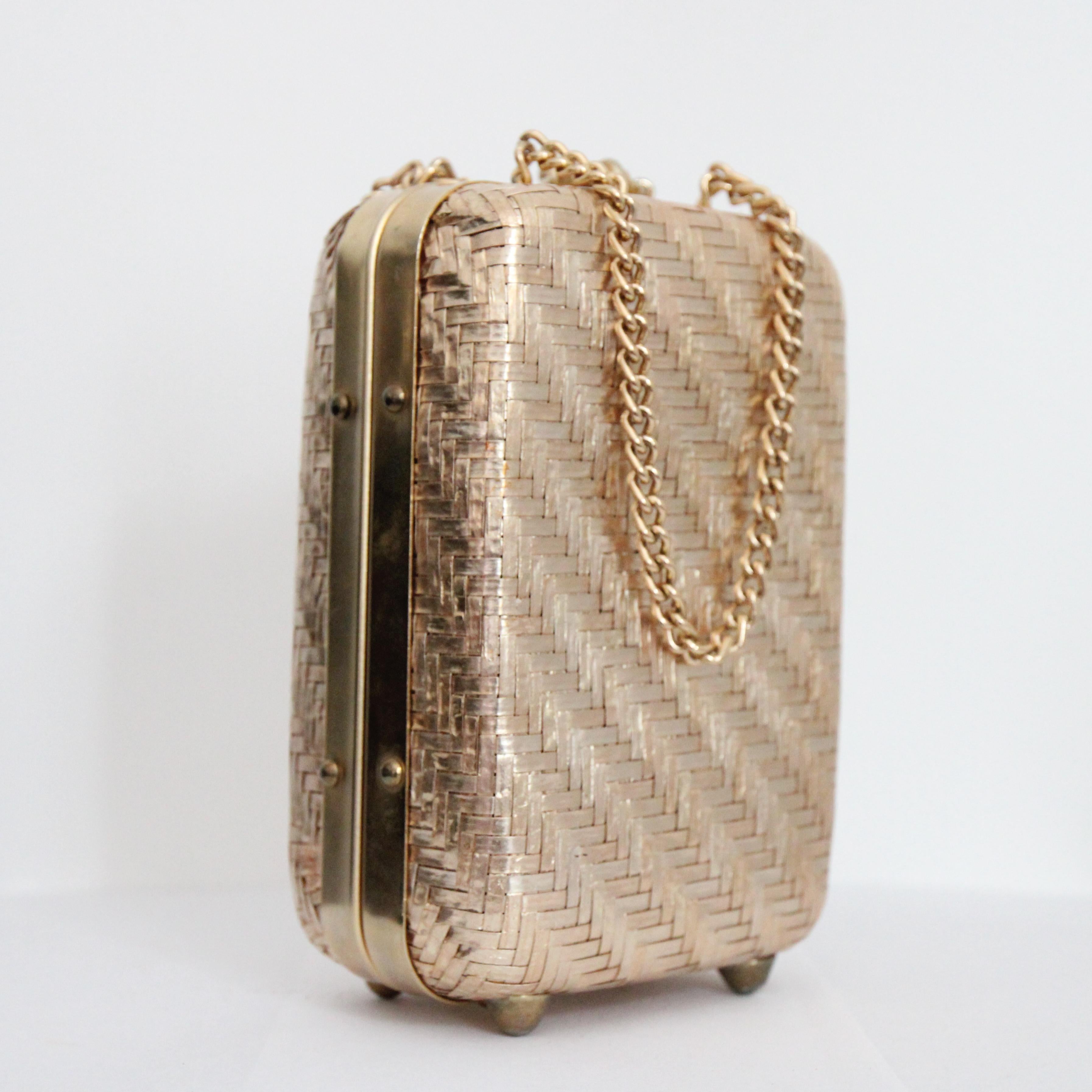  Este precioso bolso caja de paja tejida en oro metálico de los años 60, acentuado con herrajes metálicos dorados, es la pieza perfecta para añadir a tu colección de accesorios.  

La elegante forma rectangular alta presenta esquinas curvas