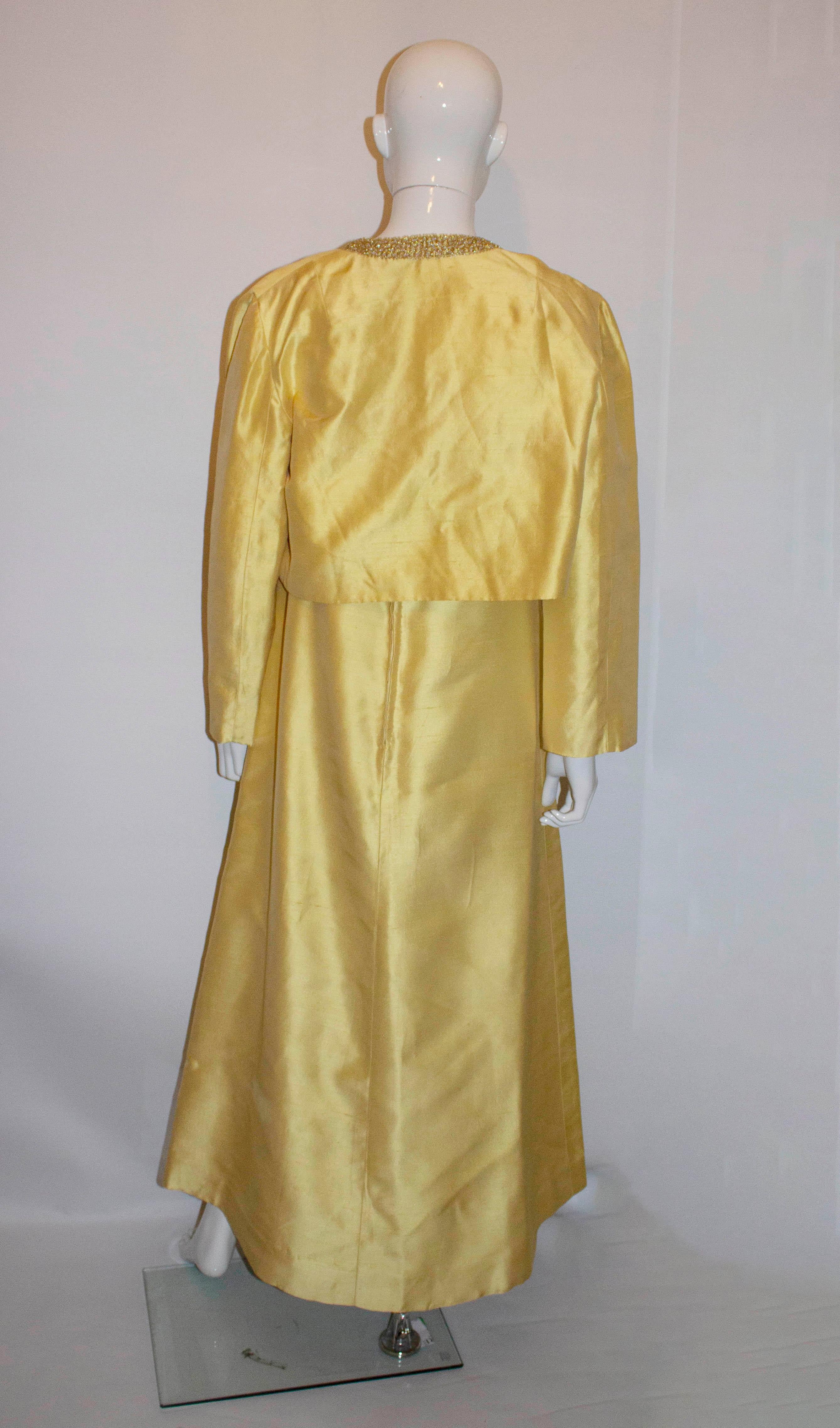 A stunning gown from the 1960s  in a sunshine yellow. The dress has a  round neckline and backline with detail under the bust. The skirt area is A line shape and the dress has a central back zip.
The matching bolero has a round neck and toggle