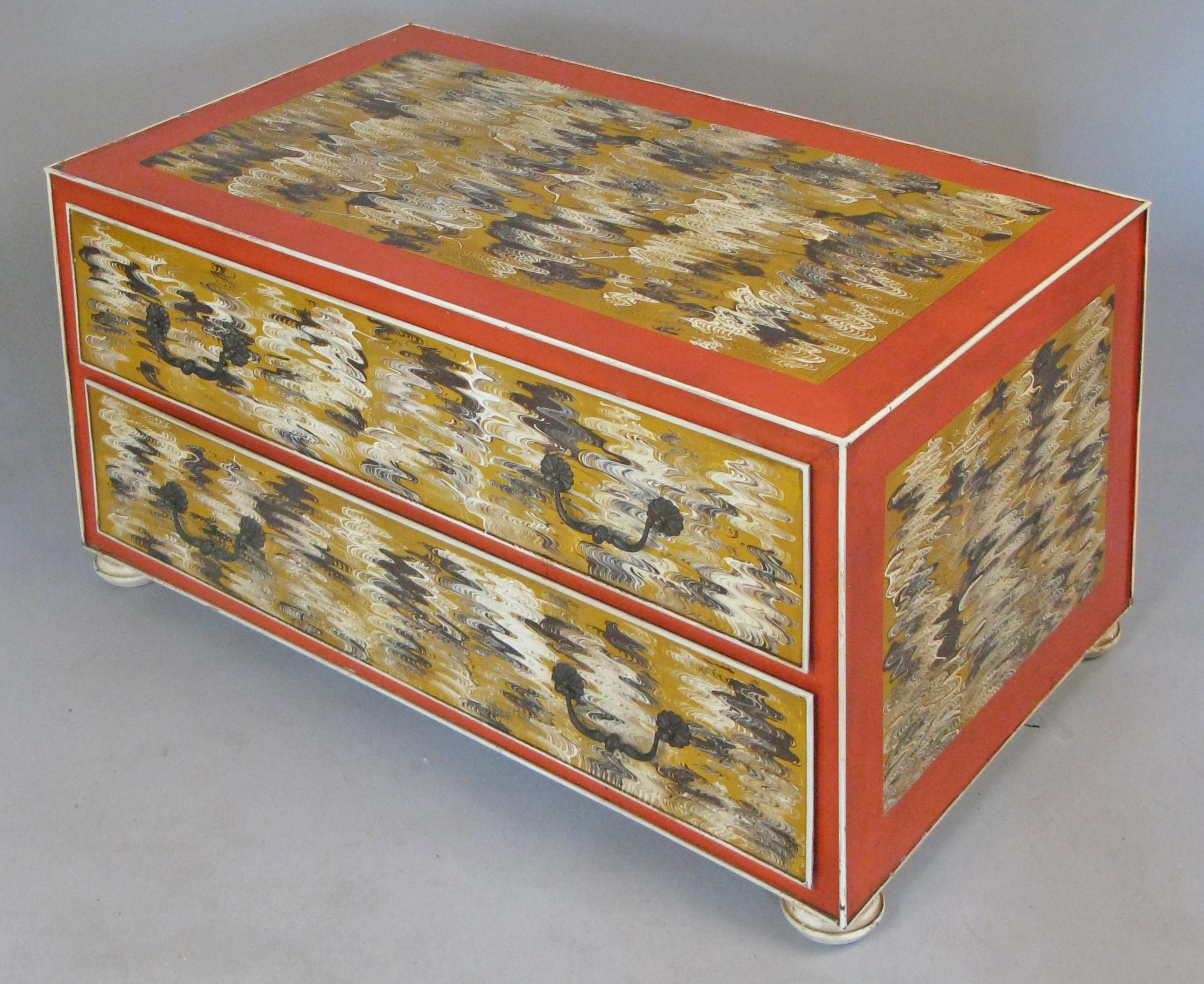 A charming vintage 1960s low metal chest, with two drawers and its original hand painted finish. The treatment has dark ochre borders with inset panels in an abstract design of beige, white, and black. Metal drawer handles and metal bun feet.