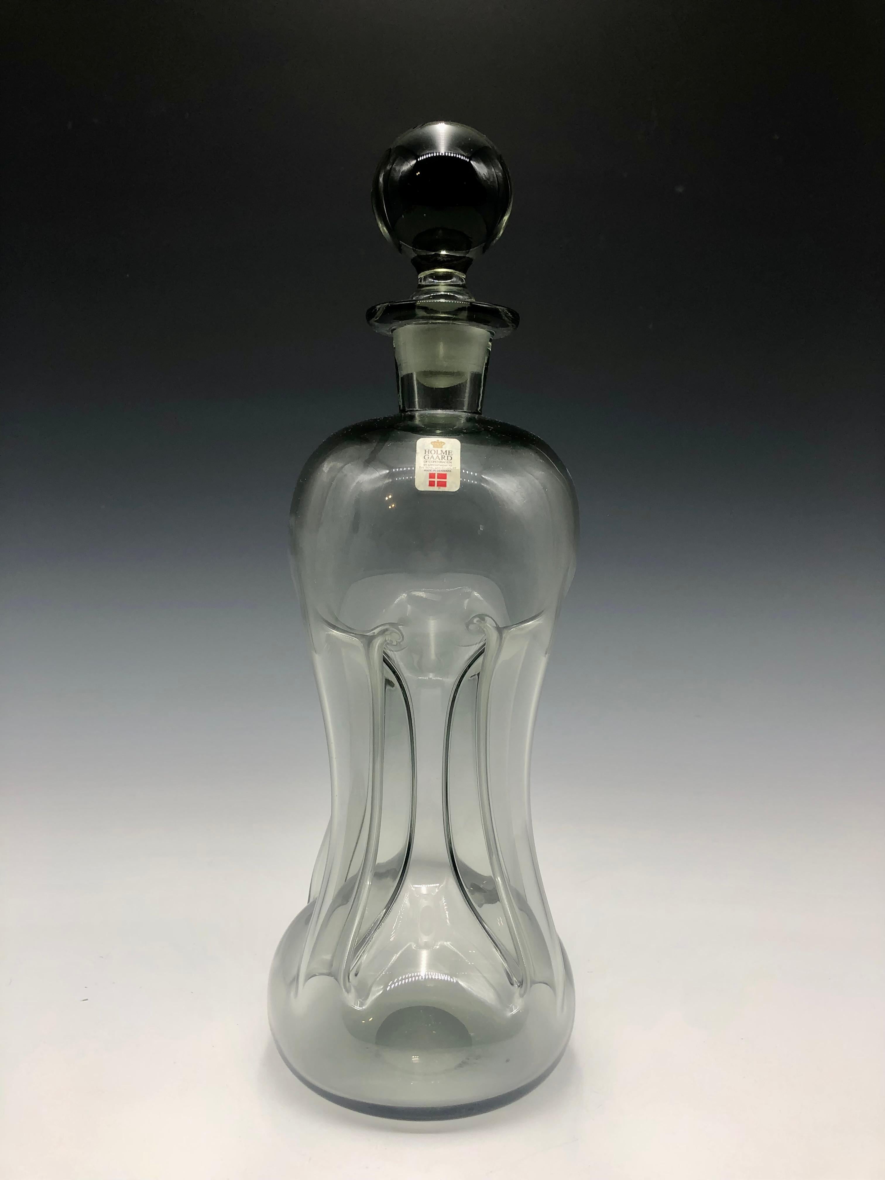 Elegant vintage mid-century Holmegaard Kluk Kluk smoke color glass decanter with stopper and original manufacturer's label by Jacob E. Bang, a true gem from 1960s Denmark. Meticulously crafted and preserved, this mouth-blown glass piece embodies the