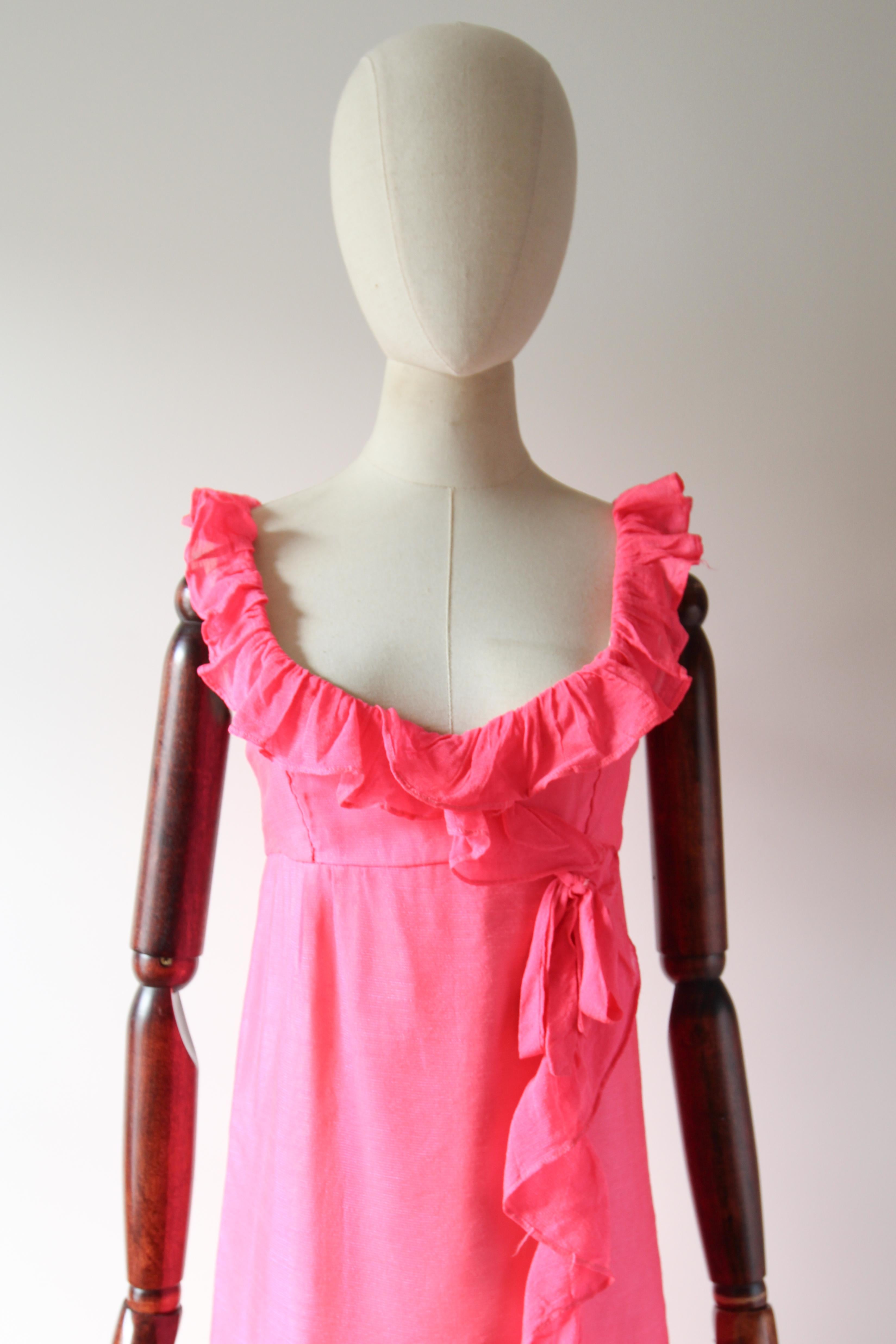 Este vibrante vestido Jean Varon de los años 60, confeccionado en el tono más brillante de algodón rosa neón, es la pieza perfecta para alegrar tu armario de temporada. 

El escote redondeado está enmarcado por una cenefa de volantes plisados en