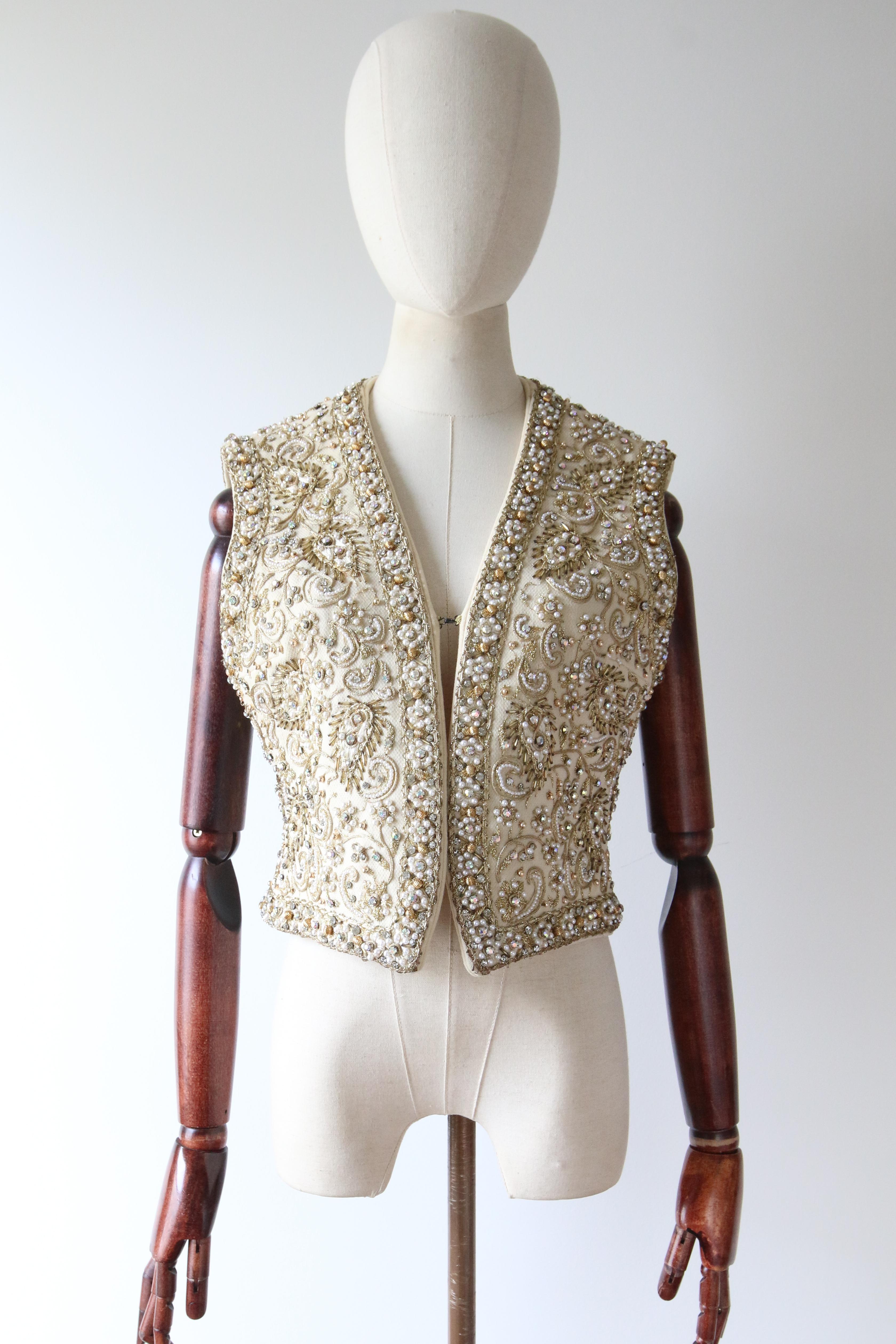 This truly magnificent 1960's waistcoat by Marie McCarthy for Larry Aldrich, rendered in a woven cream wool and embellished with trailing gold soutache embroidery, cream silk embroidery, pearlescent beads, iridescent claw set rhinestones, and silver
