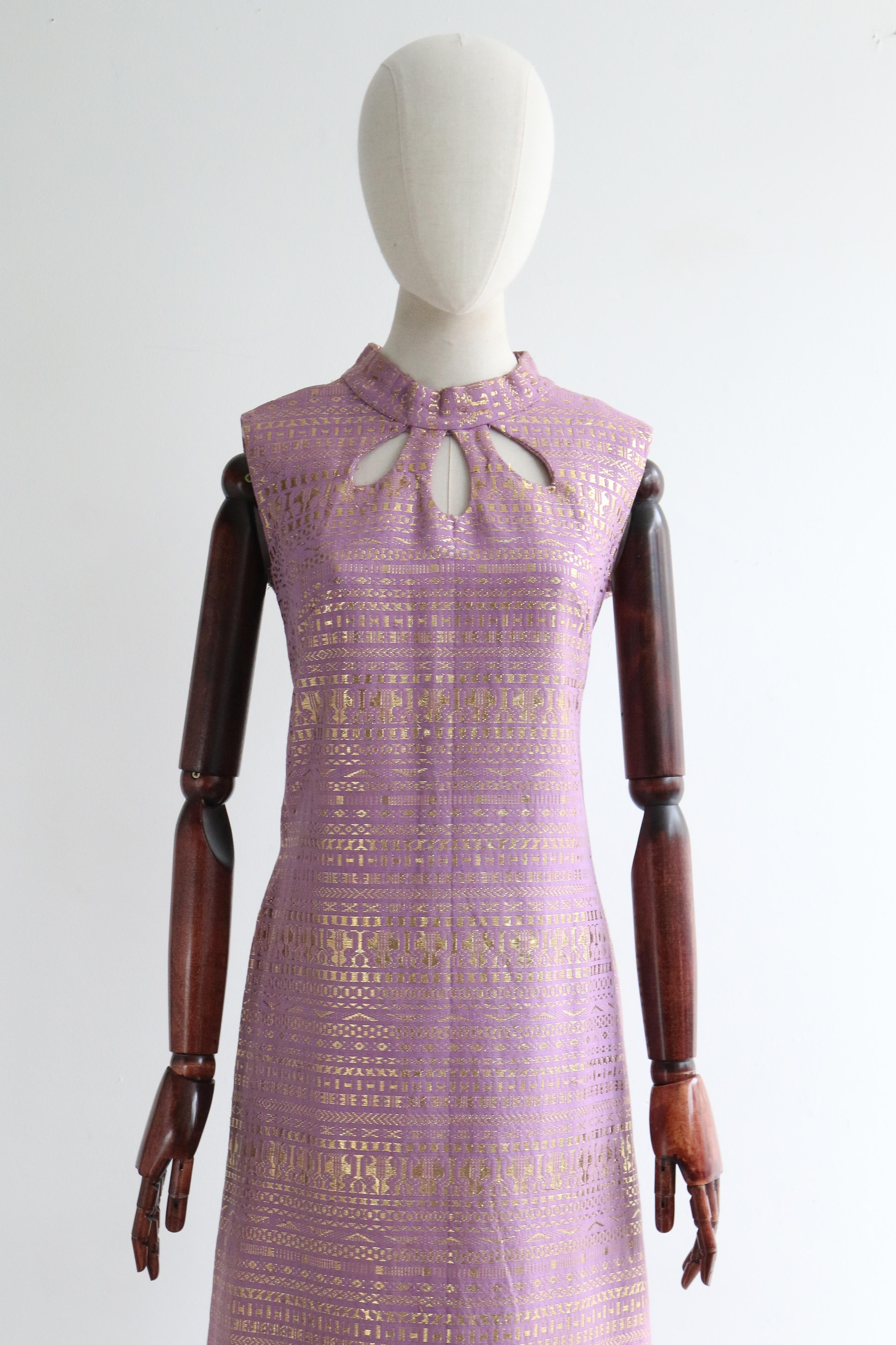 A classic silhouette rendered in a lilac cotton weave with a gold lurex thread geometric woven pattern, this eye-catching 1960's dress is just the piece for your cocktail wardrobe.  

The stylised rounded mandarin collar is framed by a simple