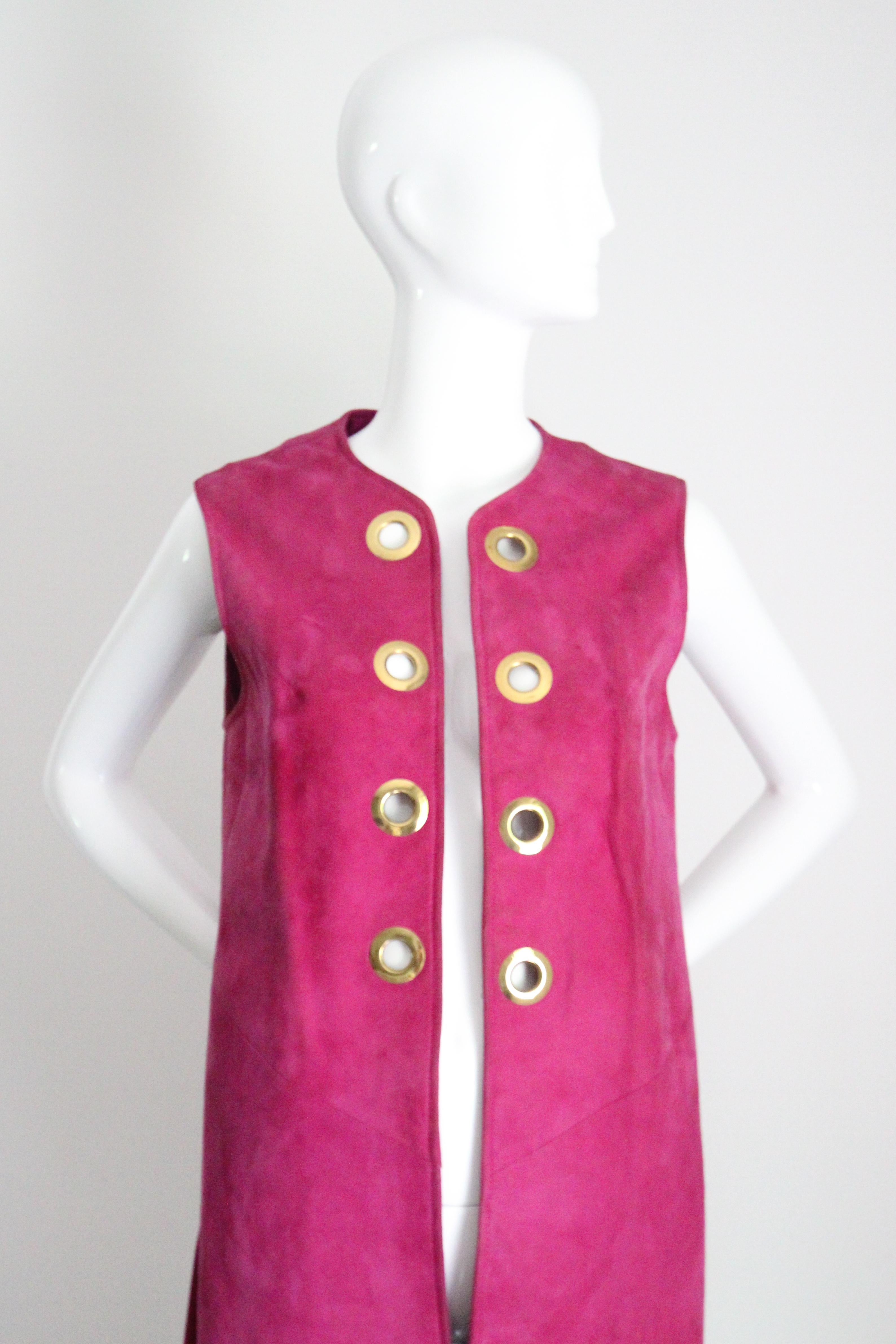 This truly eye-catching 1960's magenta suede longline waistcoat, accented by golden coloured metal eyelets,  is the perfect statement piece for your wardrobe

The rounded neckline sets off the edge to edge cut, which is decorated with 8 golden