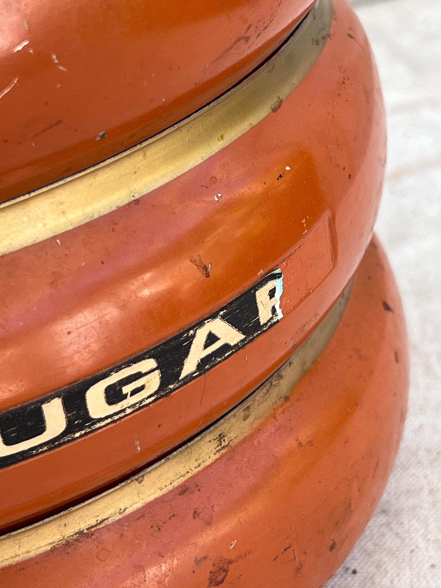 Featuring four rounded canisters, each finished in an orange enamel with a brass-tone trim, this set is topped with a matching lid and a decorative finial. The canisters stack neatly to form a practical storage solution. Perfect for organizing dry