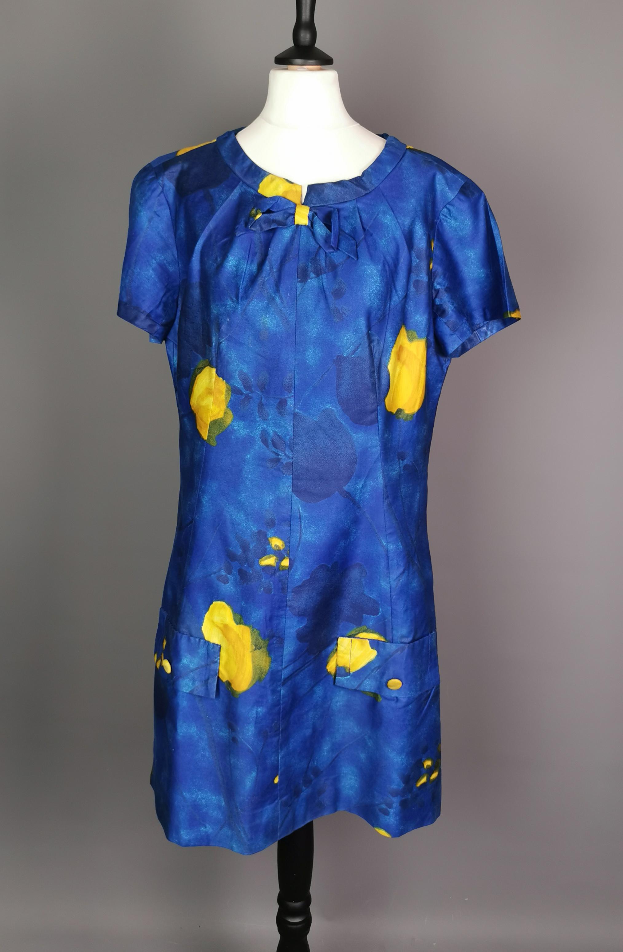 A fantastic vintage late c1960s Mod mini dress.

It is made from a synthetic cotton blend, nipped in waist with an A line skirt in a vibrant blue witb with a yellow pattern, very colourful.

It has a round crew neck with a sweet bow.

The dress has