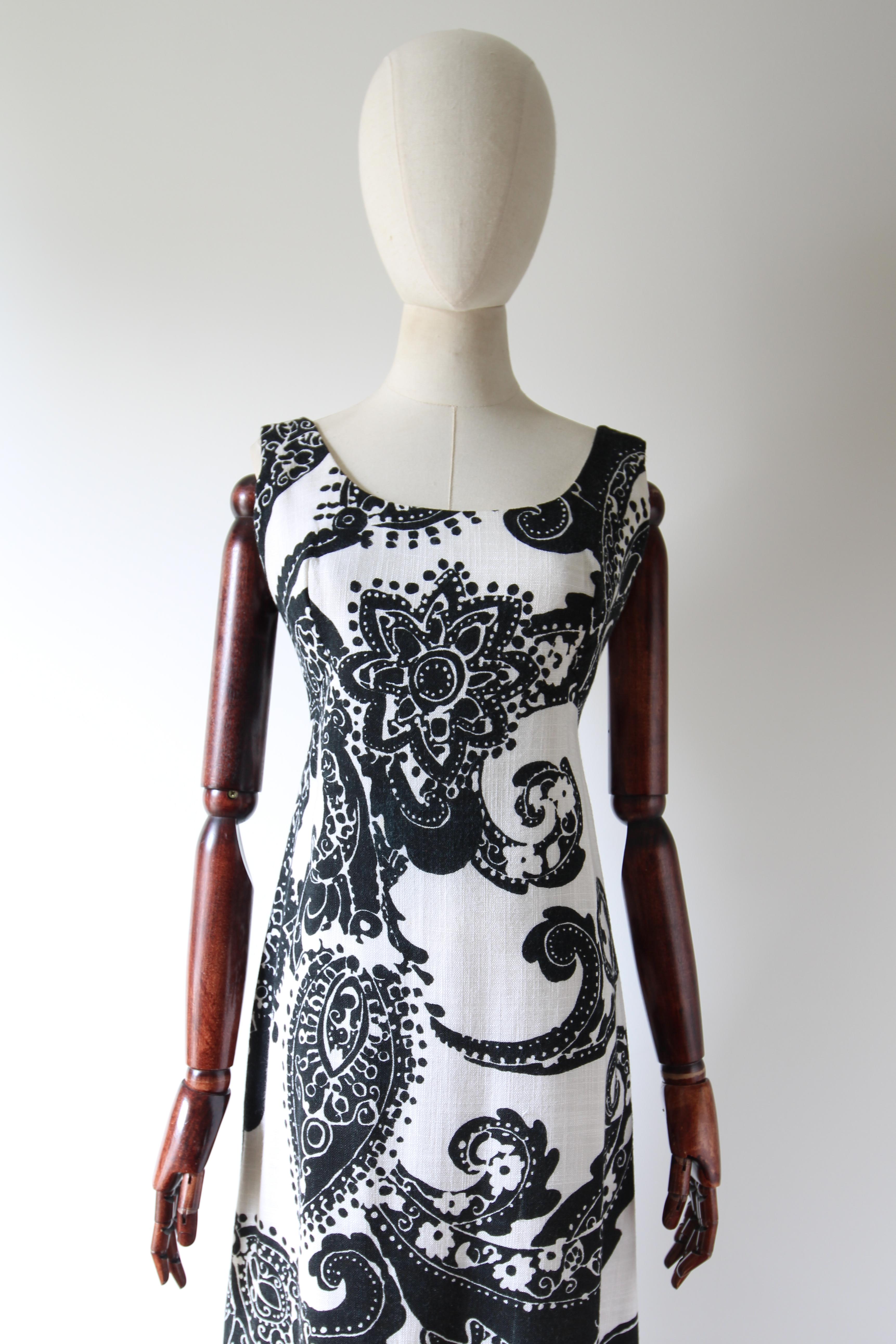 Questo abito originale degli anni '60, realizzato in lino bianco spesso con un motivo decorativo monocromatico nero, è il pezzo giusto per il tuo guardaroba stagionale. 

La scollatura arrotondata è incorniciata da spalline medie e da un taglio