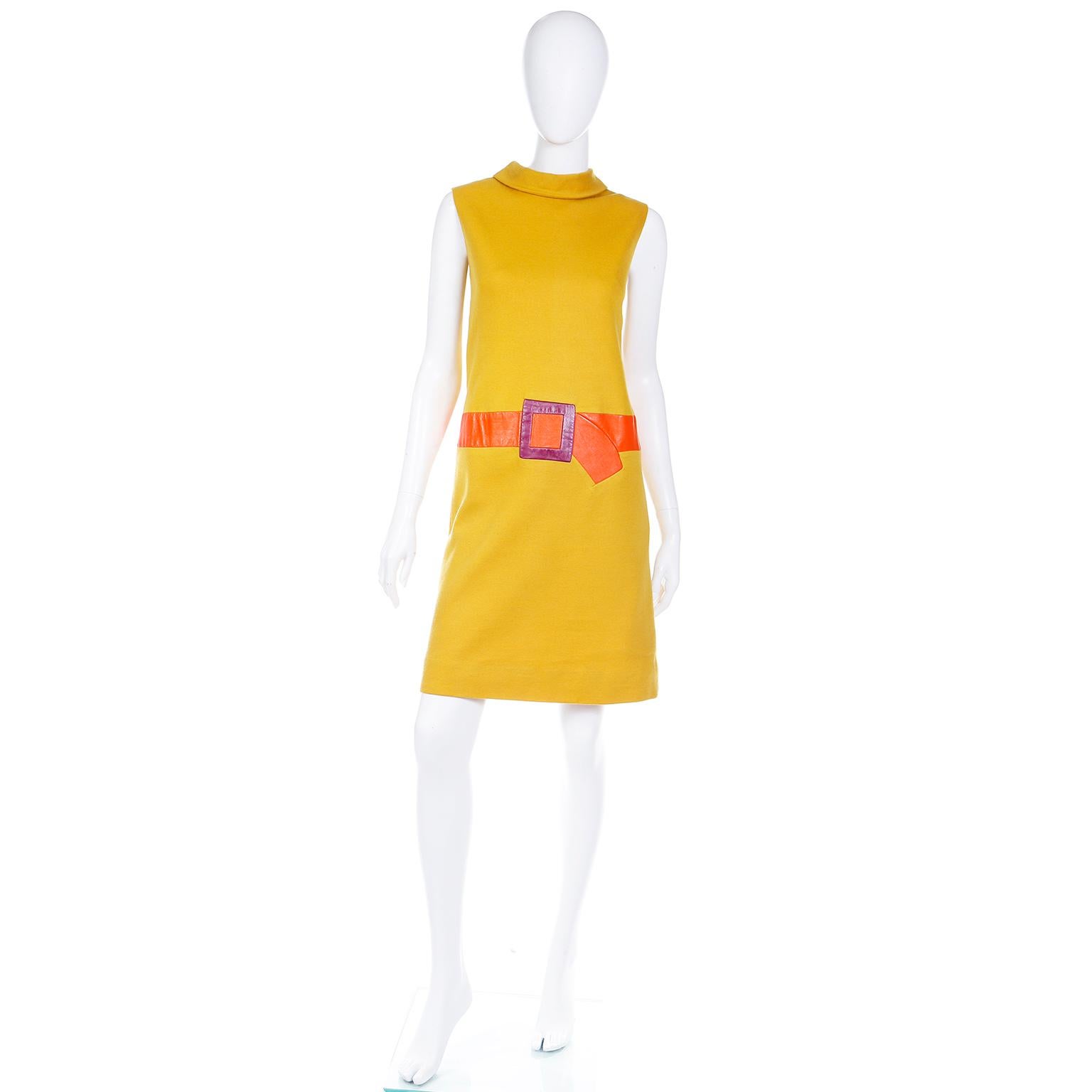 This is a really fun vintage late 1960's or early 1970's mustard yellow trompe l'oeil 2 piece dress suit This fabulous outfit includes a mustard yellow sleeveless mock turtleneck shift dress with a leather faux orange belt with a purple buckle.  The