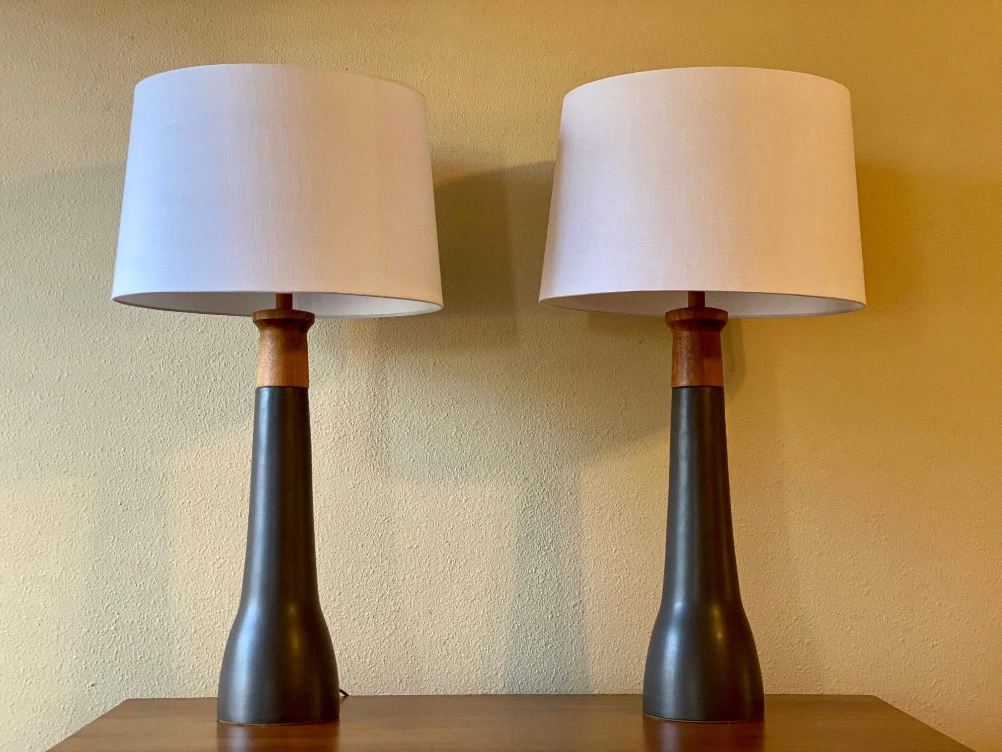Elegant pair of walnut and ceramic table lamps designed by husband and wife duo Jane & Gordon Martz. Produced by Marshall Studios, Indiana. Lamps feature a lovely matte black/gunmetal glaze with figured walnut necks and finials. New harps and